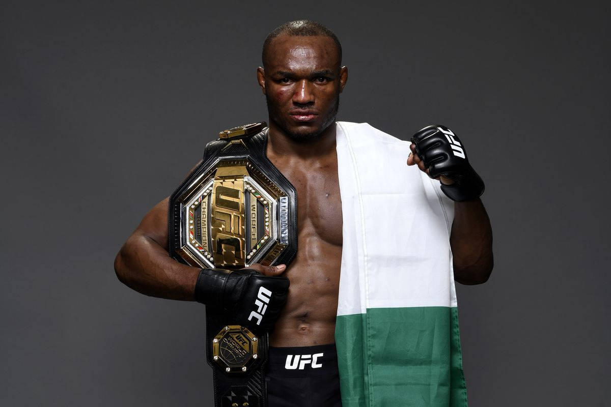 Nigeria 桌布 壁紙 — 一位肌肉發達的UFC拳手在黑暗的攝影棚背景下，披著奈及利亞國旗，手持冠軍腰帶。