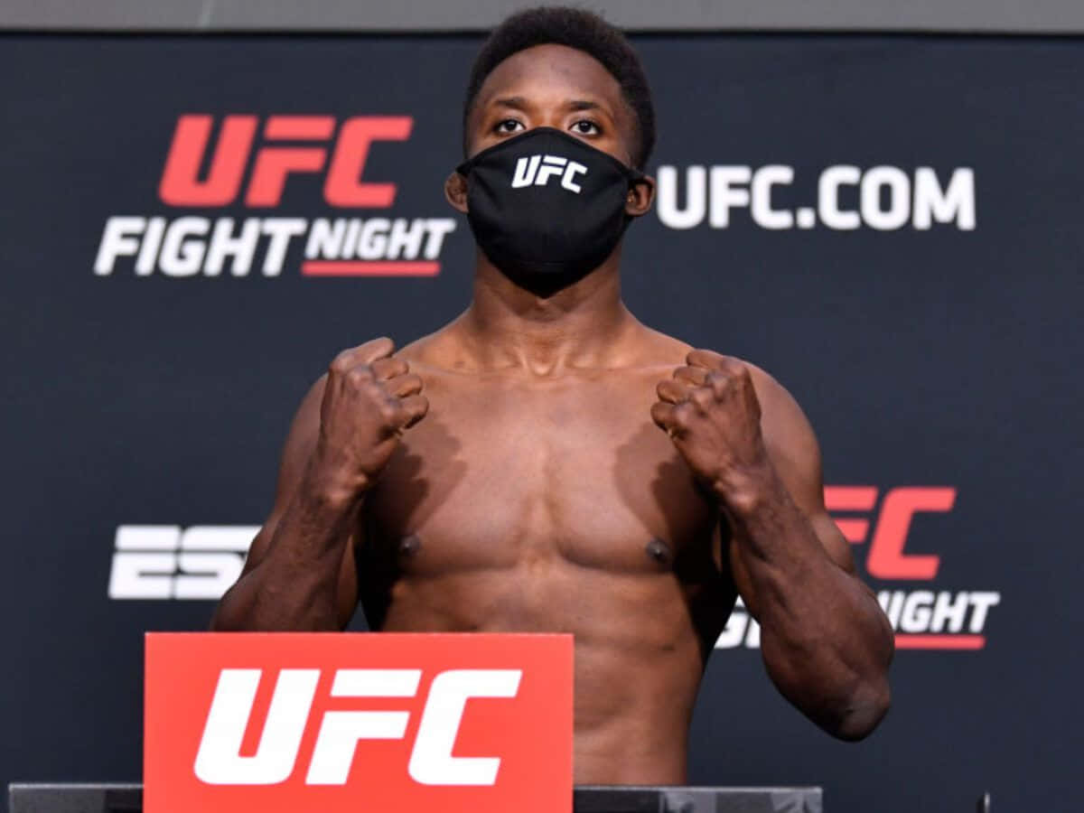 MMA 桌布 壁紙 — 一位肌肉發達的UFC拳手戴著黑色口罩，在UFC品牌背景的稱重活動中握拳。
