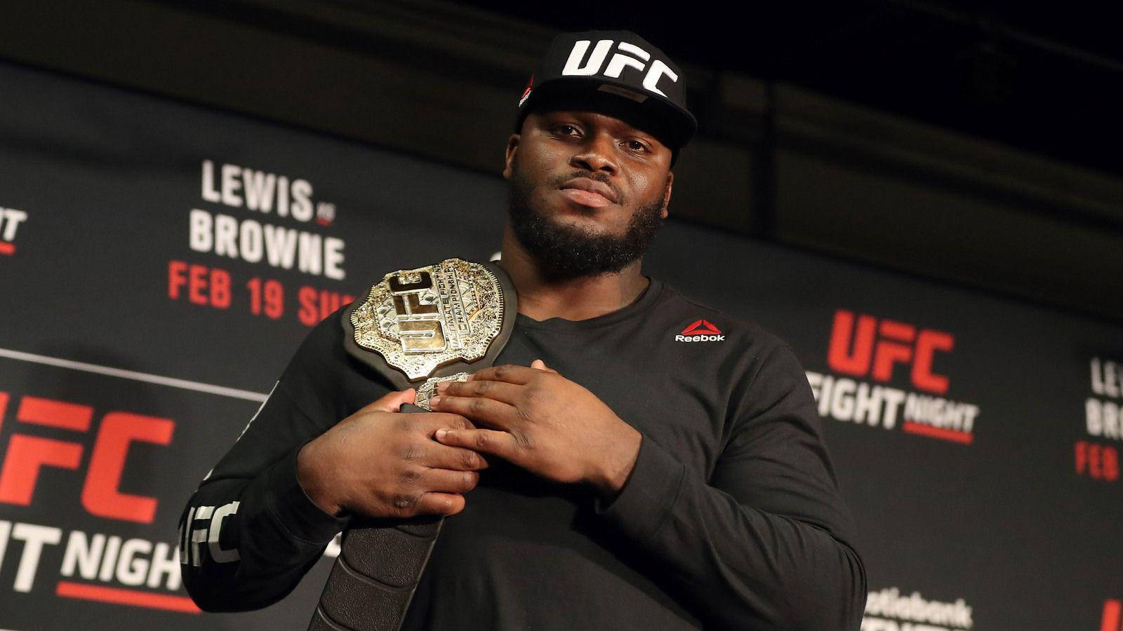 UFC 桌布 壁紙 — 一位肌肉發達的UFC拳手戴著黑色帽子和襯衫，在記者會上自豪地舉起冠軍腰帶。