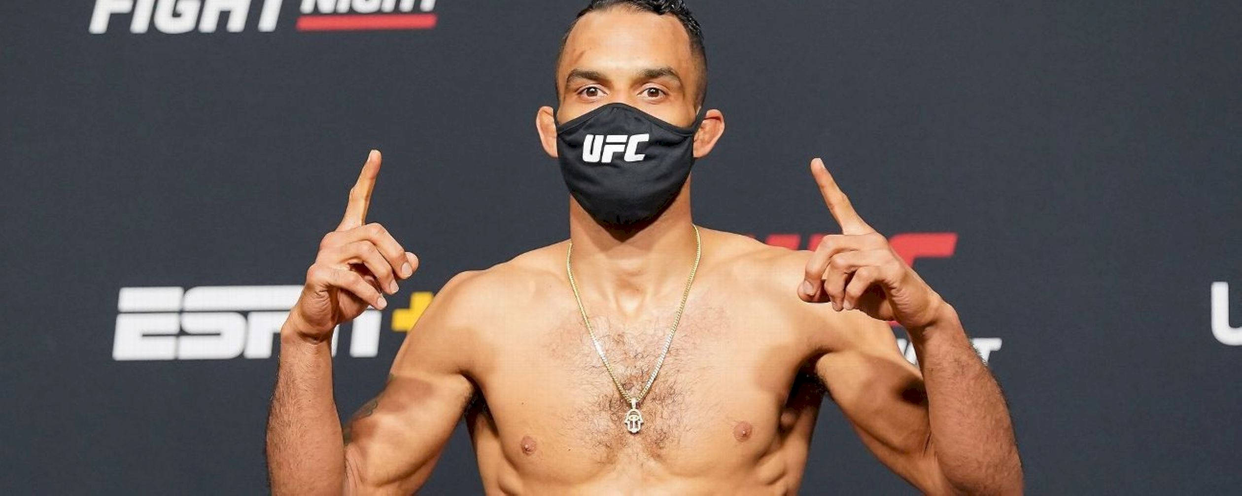MMA 桌布 壁紙 — 一位肌肉發達的UFC拳手戴著黑色面罩，在深色品牌背景前用雙食指向上指。