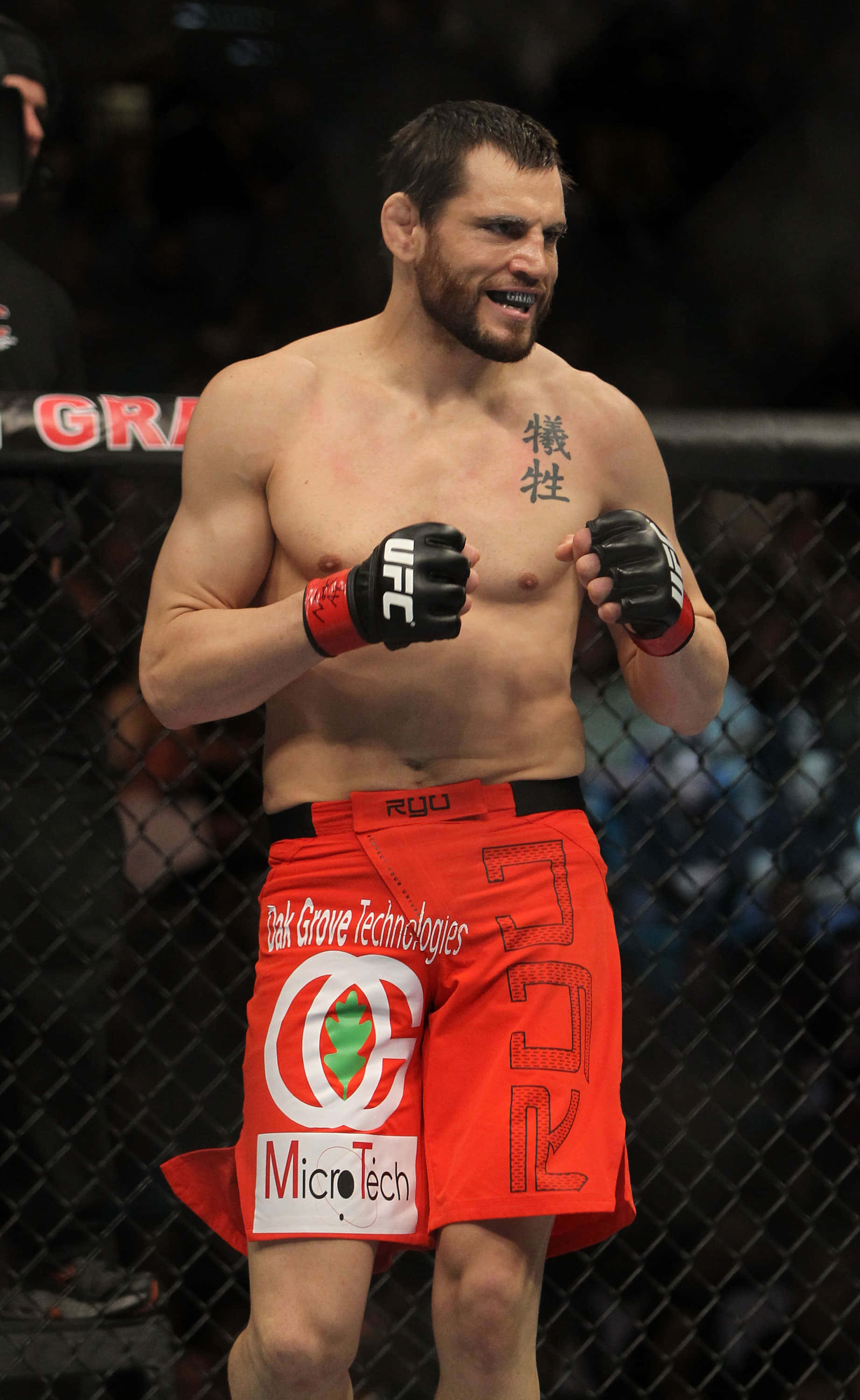UFC 桌布 壁紙 — 一位肌肉發達的UFC拳手穿著紅色短褲，在八角籠內帶著兇猛的笑容和紋身胸膛慶祝。