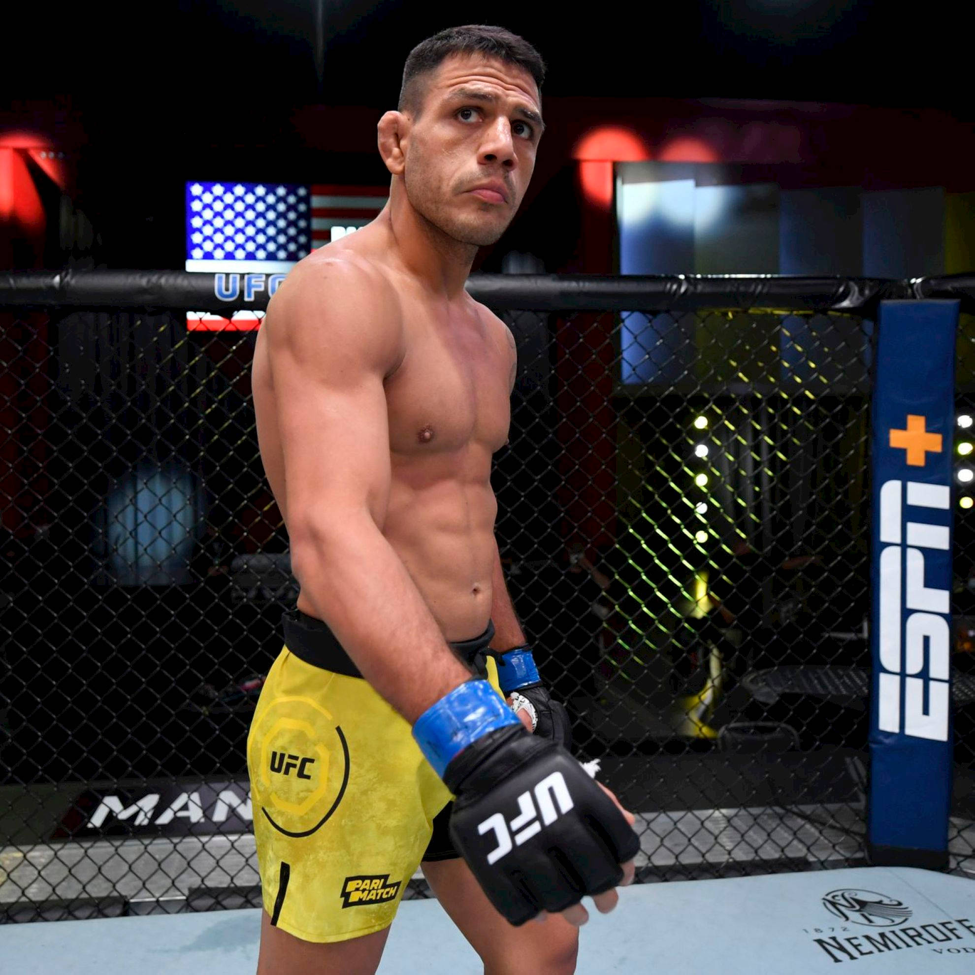 UFC 桌布 壁紙 — 一位肌肉發達的UFC拳手穿著黃色短褲，在場館燈光下專注地站在八角籠內。