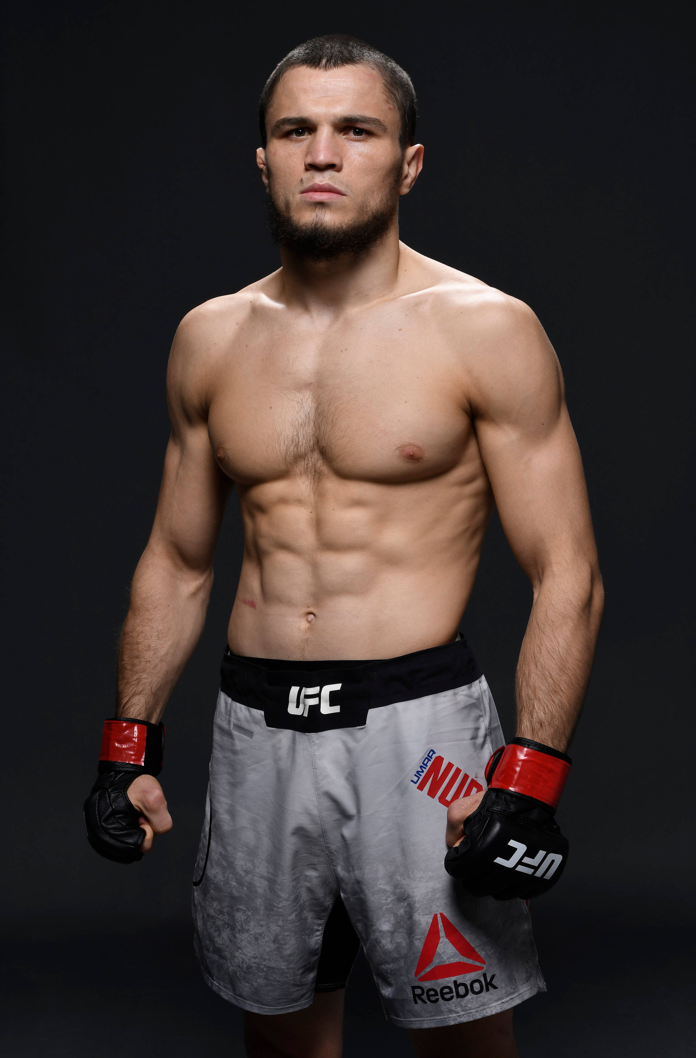 UFC 桌布 壁紙 — 一位肌肉發達的UFC拳手自信地穿著格鬥短褲和手套，站在深色工作室背景前。