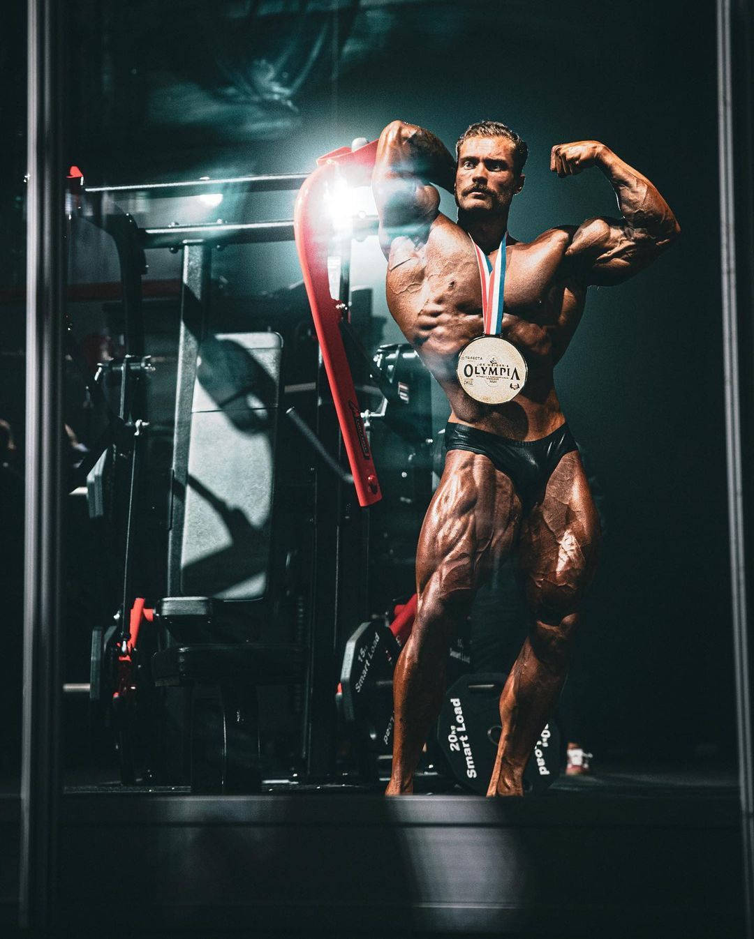 健美運動員在聚光燈下於舞台上手持紅色毛巾和奧林匹亞獎牌。 — 健身房 壁紙