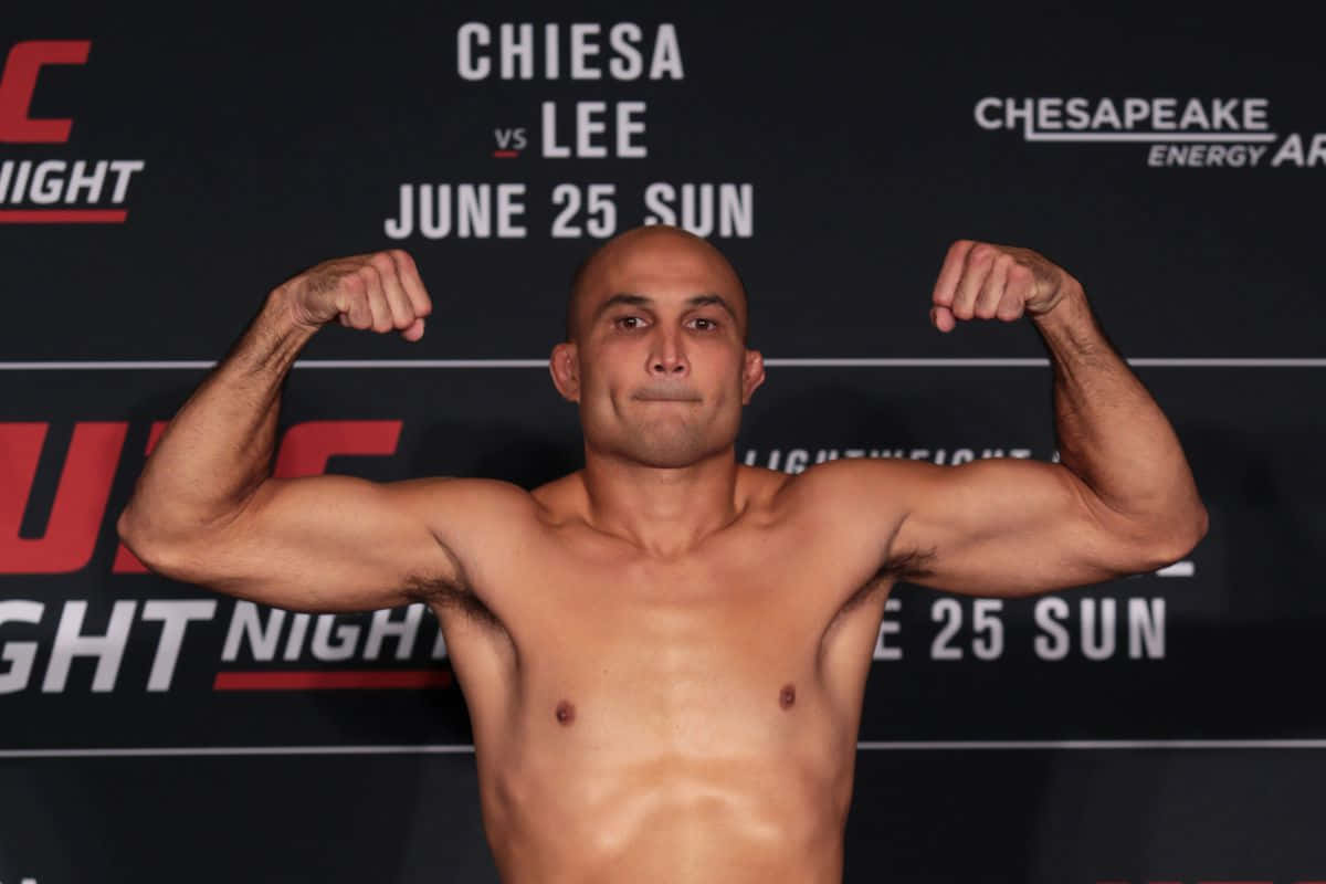 MMA 桌布 壁紙 — 一位肌肉發達的光頭拳擊手在UFC稱重活動中彎曲雙臂，身後有宣傳文字。