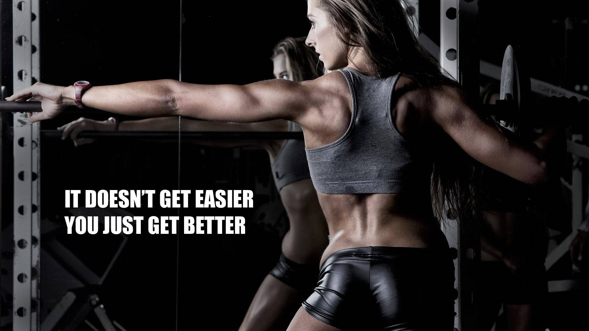 Fitness 桌布 壁紙 — 一位肌肉發達的女性在健身房中，在戲劇性的燈光下，以高度專注的狀態進行槓鈴划船。