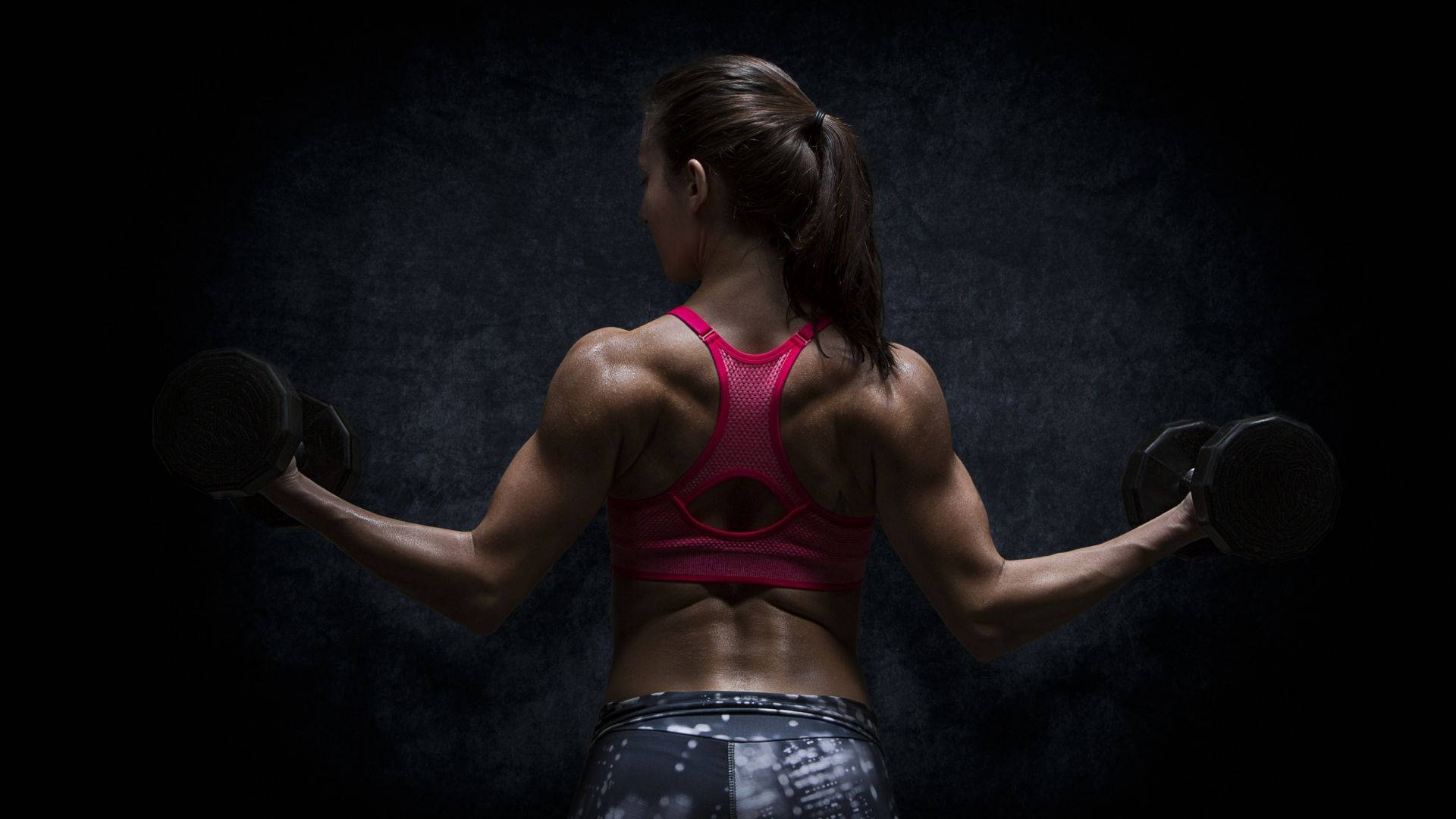 muscle growth 桌布 壁紙 — 一位肌肉發達的女性穿著粉紅色運動內衣，在黑暗紋理背景和戲劇性燈光下舉起啞鈴。