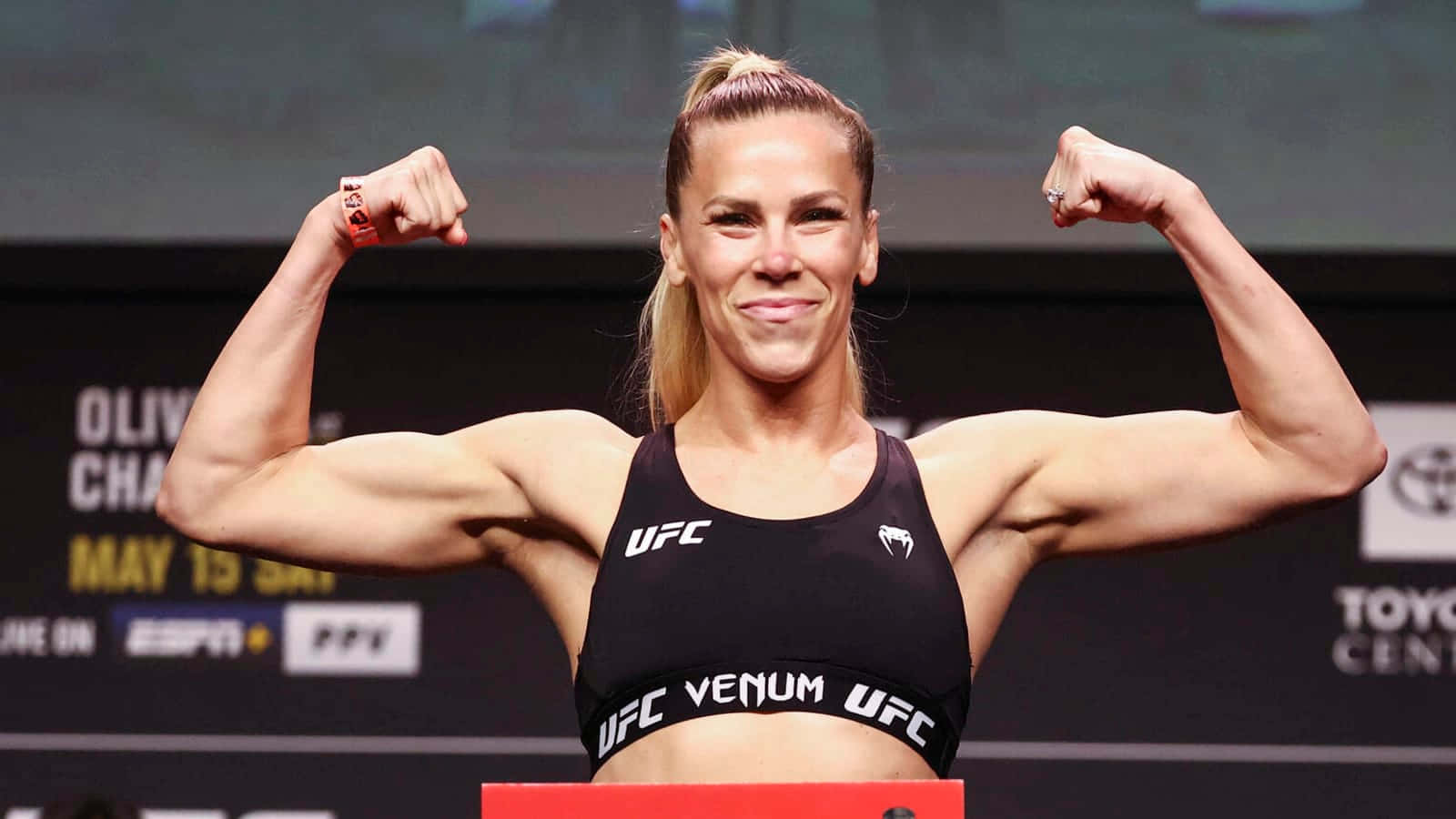 桌布 壁紙 — 一位肌肉發達的女拳手在UFC稱重活動中自信地微笑並彎曲雙臂。