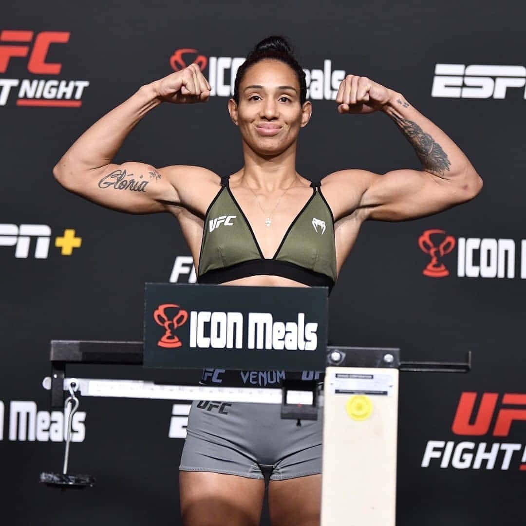 MMA 桌布 壁紙 — 一位肌肉發達的女拳手在帶有品牌背景的UFC稱重台上自信地彎曲手臂。