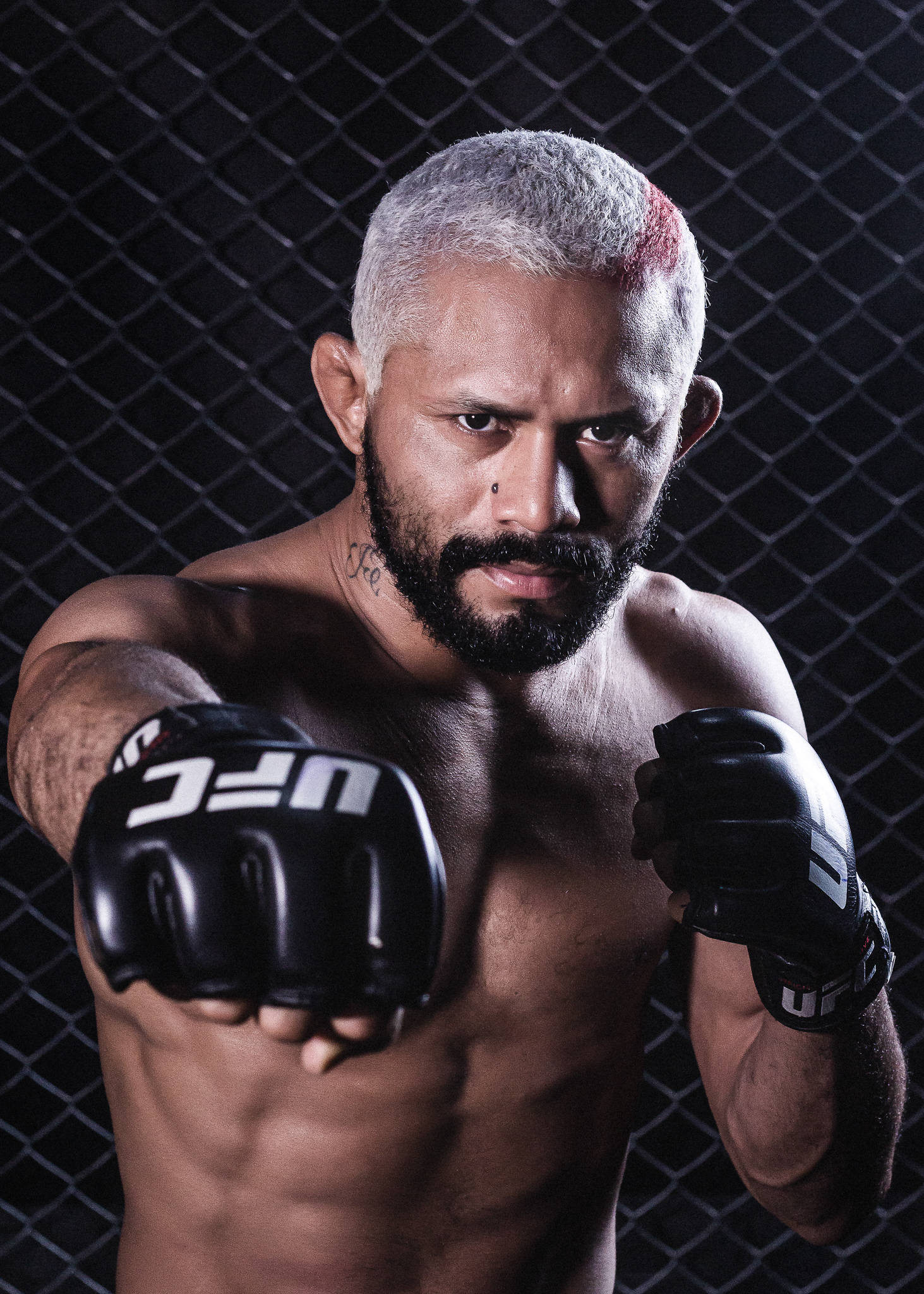 MMA 桌布 壁紙 — 一位肌肉發達的戰士，銀色頭髮帶有紅色條紋，透過UFC手套在深色鐵絲網前凝視。