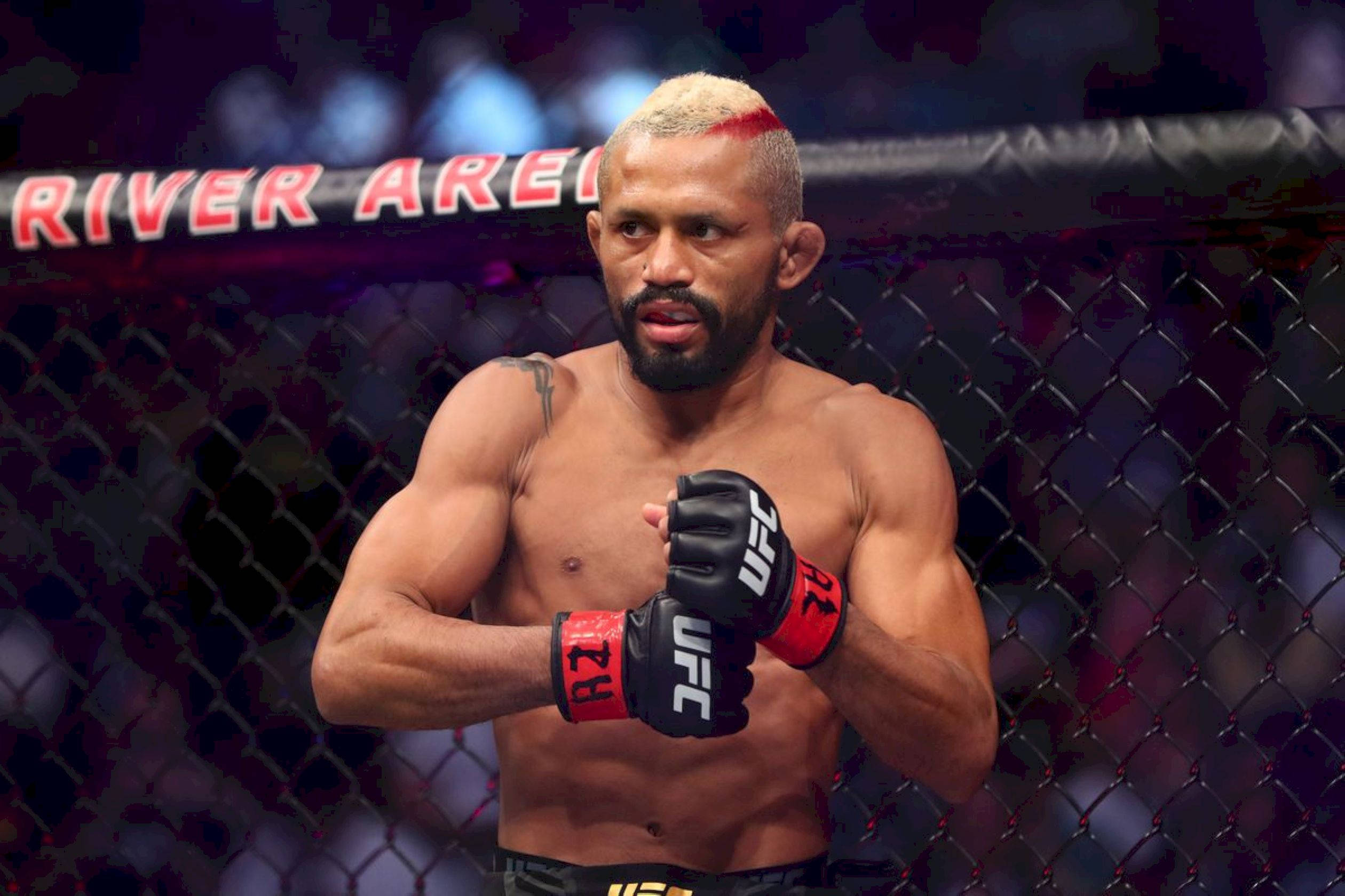 UFC 桌布 壁紙 — 一位肌肉發達的戰士，頭髮上有一條紅色條紋，站在UFC八角籠內，戴著黑色和紅色的手套。