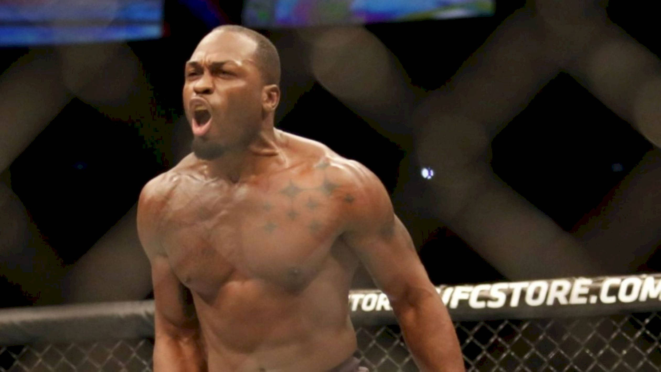 Athletic 桌布 壁紙 — 一位肌肉發達的戰士在UFC八角籠內，背後是模糊的人群和明亮的燈光，發出勝利的咆哮。