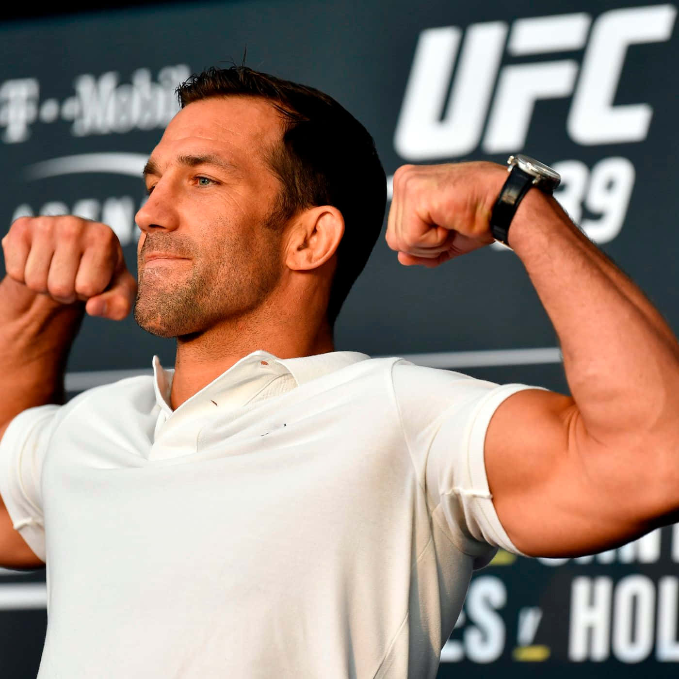 UFC 桌布 壁紙 — 一位肌肉發達的戰士在UFC活動中穿著白色Polo衫，雙臂彎曲，背景帶有品牌標誌。