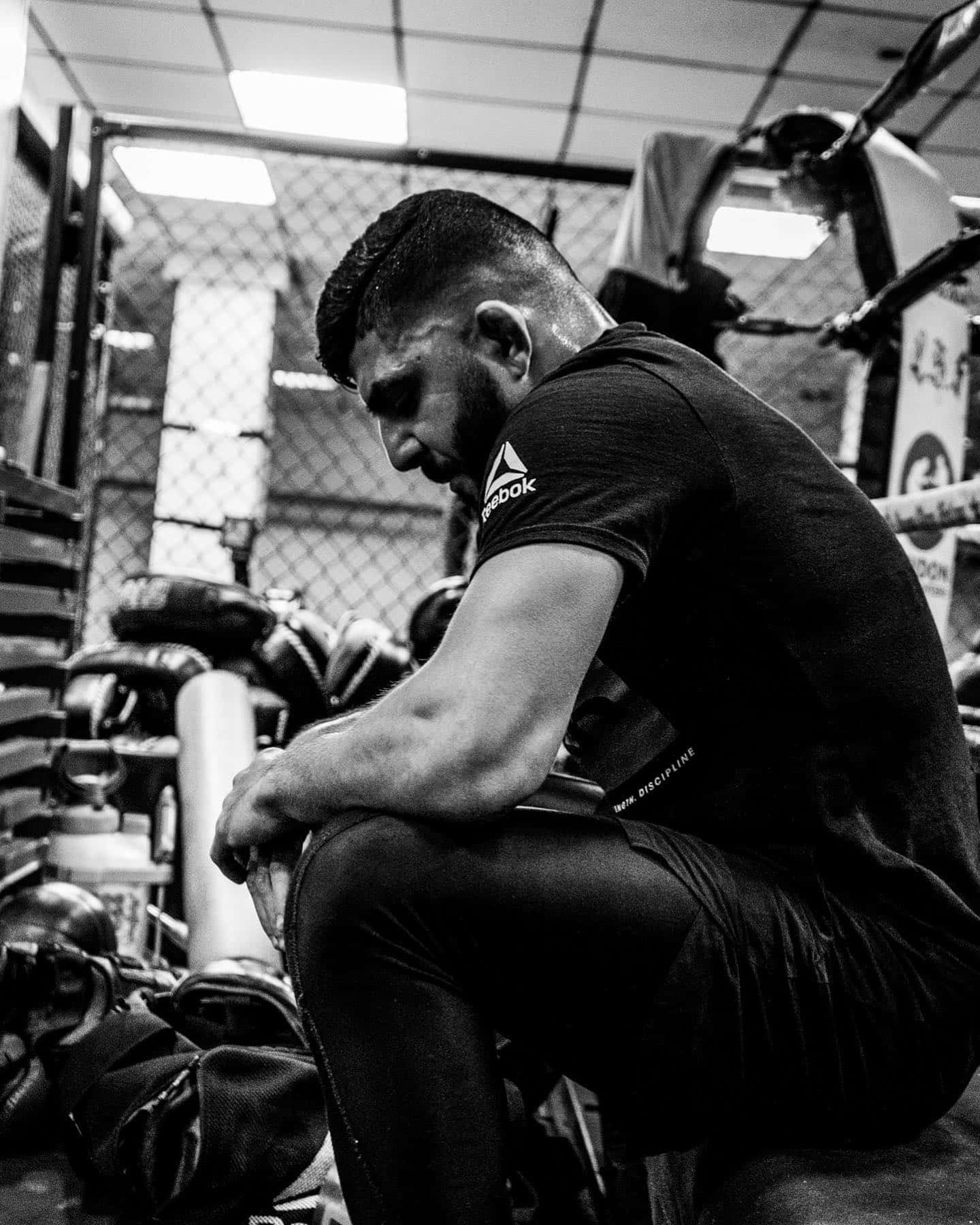 Fitness 桌布 壁紙 — 一位肌肉發達的戰士在昏暗的健身房中沉思，周圍是訓練器材和沙包。
