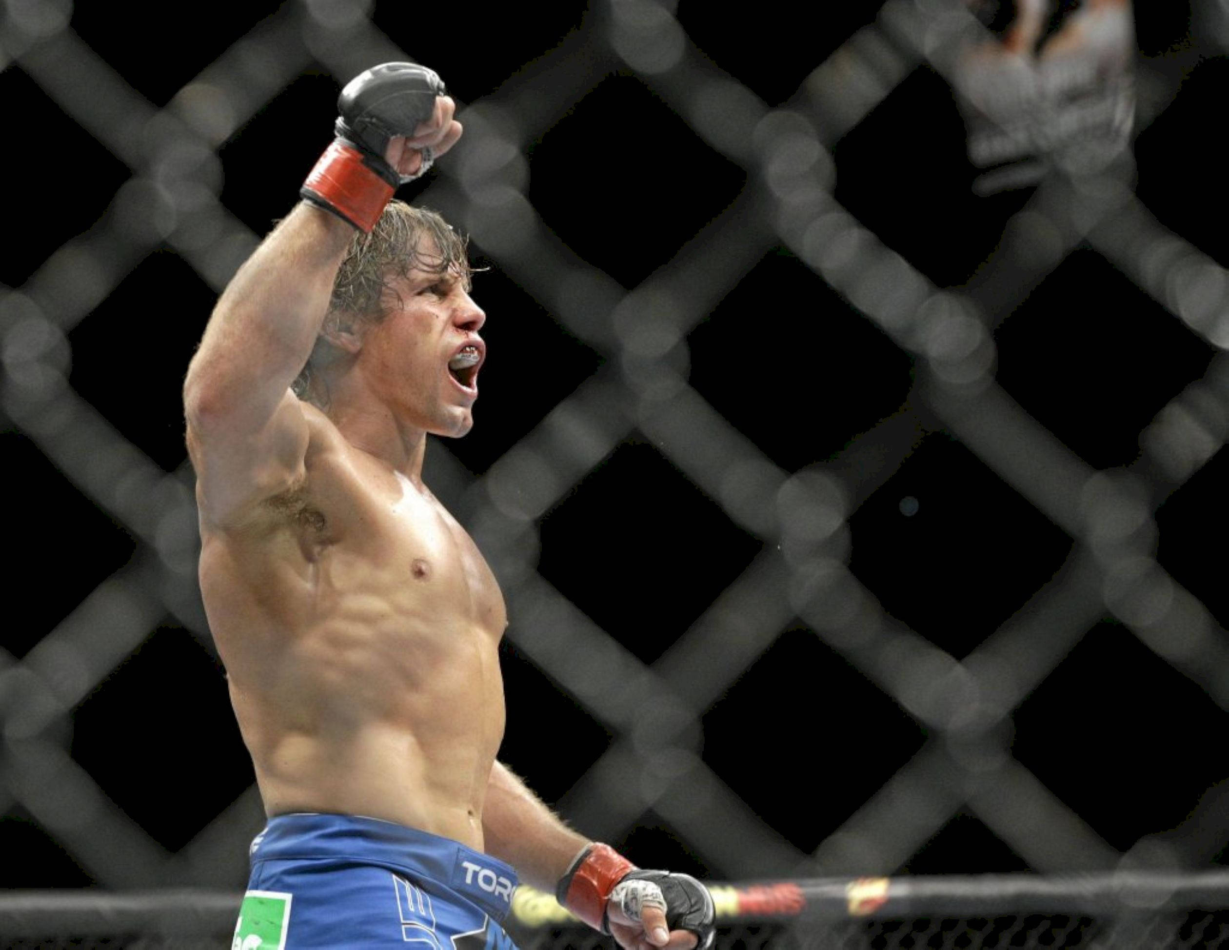 UFC 桌布 壁紙 — 一位肌肉發達的戰士在昏暗的八角籠內高舉拳頭，發出勝利的怒吼。