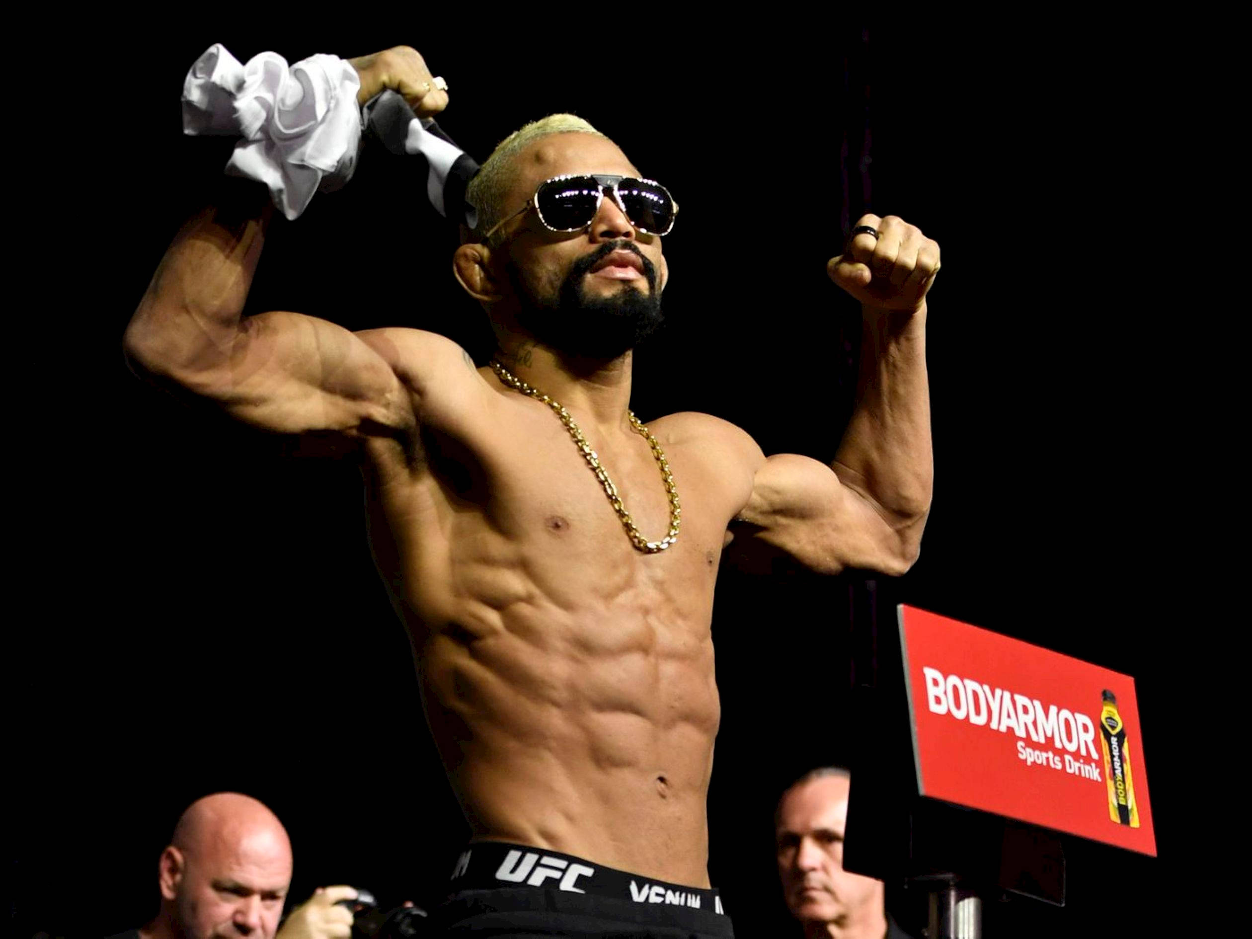 MMA 桌布 壁紙 — 一位肌肉發達的戰士戴著太陽眼鏡和UFC短褲，在明亮的場館燈光下用毛巾擦汗，得意地展示肌肉。