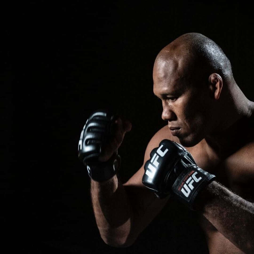 martial arts 桌布 壁紙 — 一位肌肉發達的戰士戴著黑色UFC手套，在戲劇性燈光下，在純黑背景前擺出專注的姿勢。