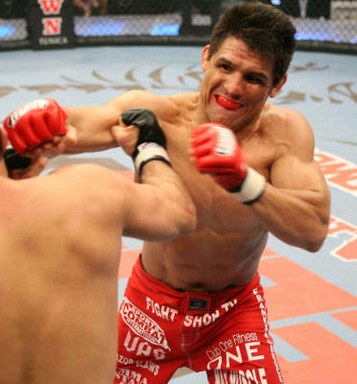 MMA 桌布 壁紙 — 一位肌肉發達的戰士穿著紅色短褲，在八角籠內激烈的綜合格鬥比賽中打出強力一拳。
