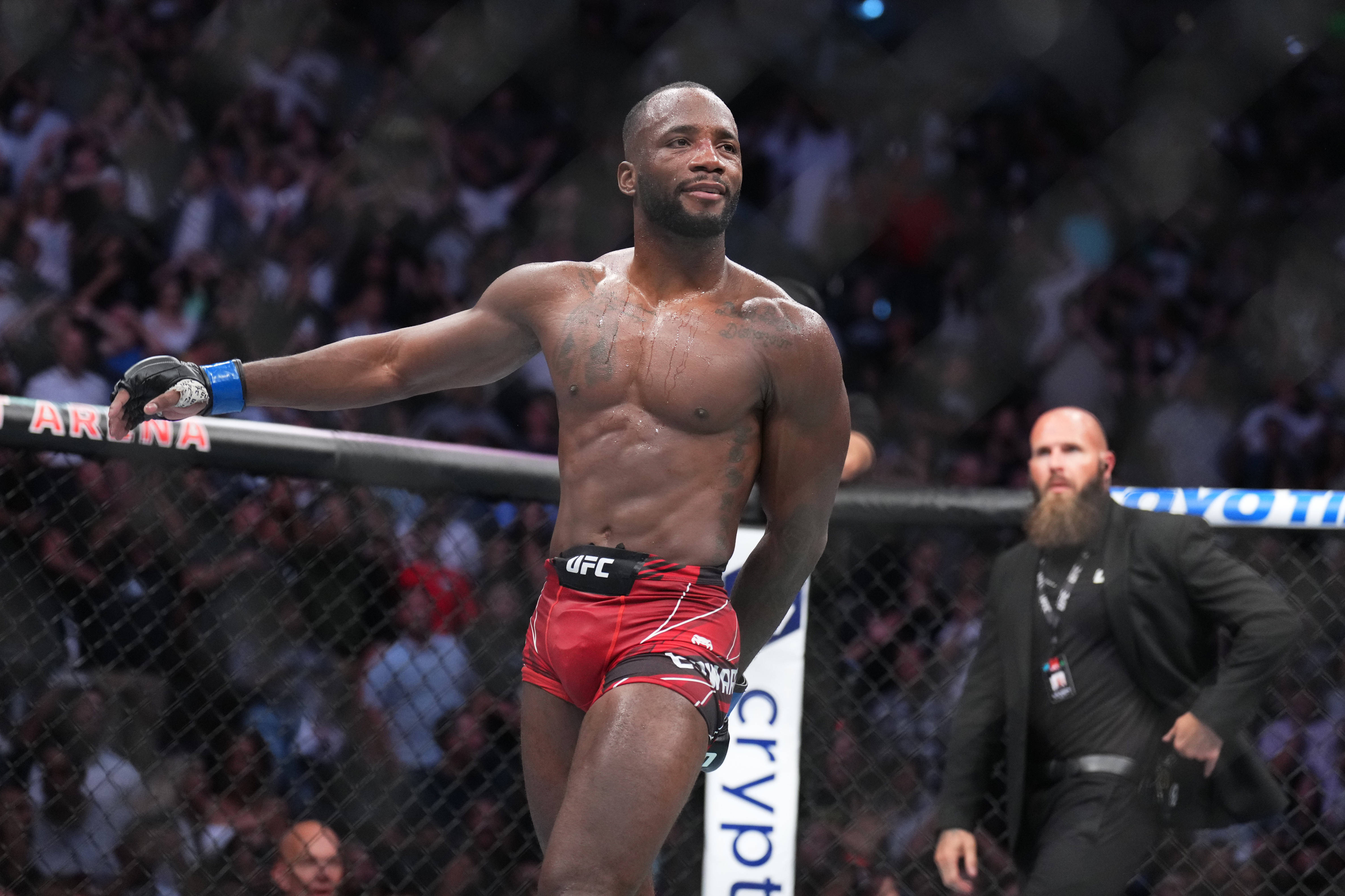 MMA 桌布 壁紙 — 一位肌肉發達的戰士穿著紅色短褲，在UFC八角籠中張開雙臂勝利站立，人群在圍欄後歡呼。