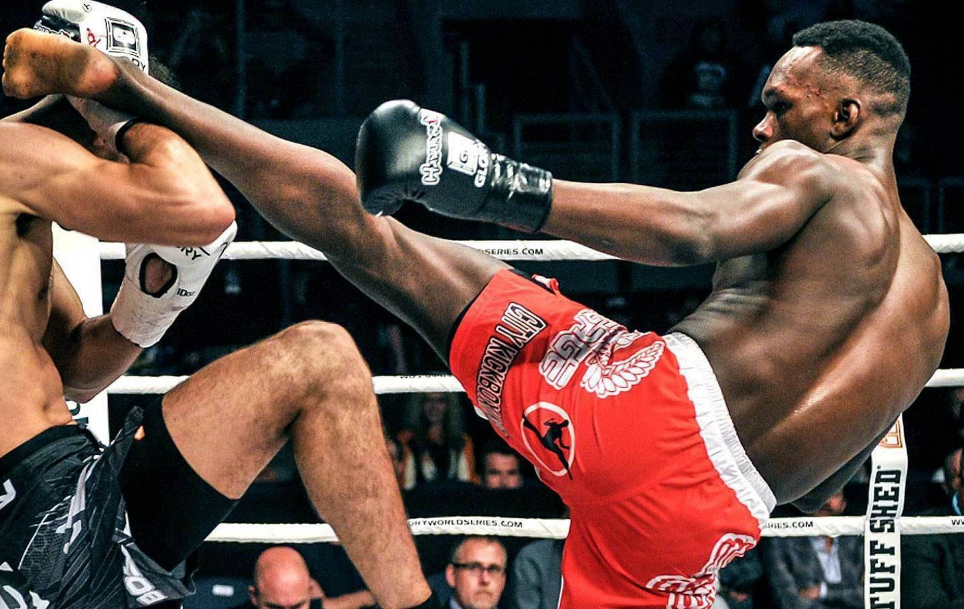 Boxing 桌布 壁紙 — 一位肌肉發達的戰士穿著紅色短褲，在燈光昏暗的拳擊場中向對手發出強力高踢。