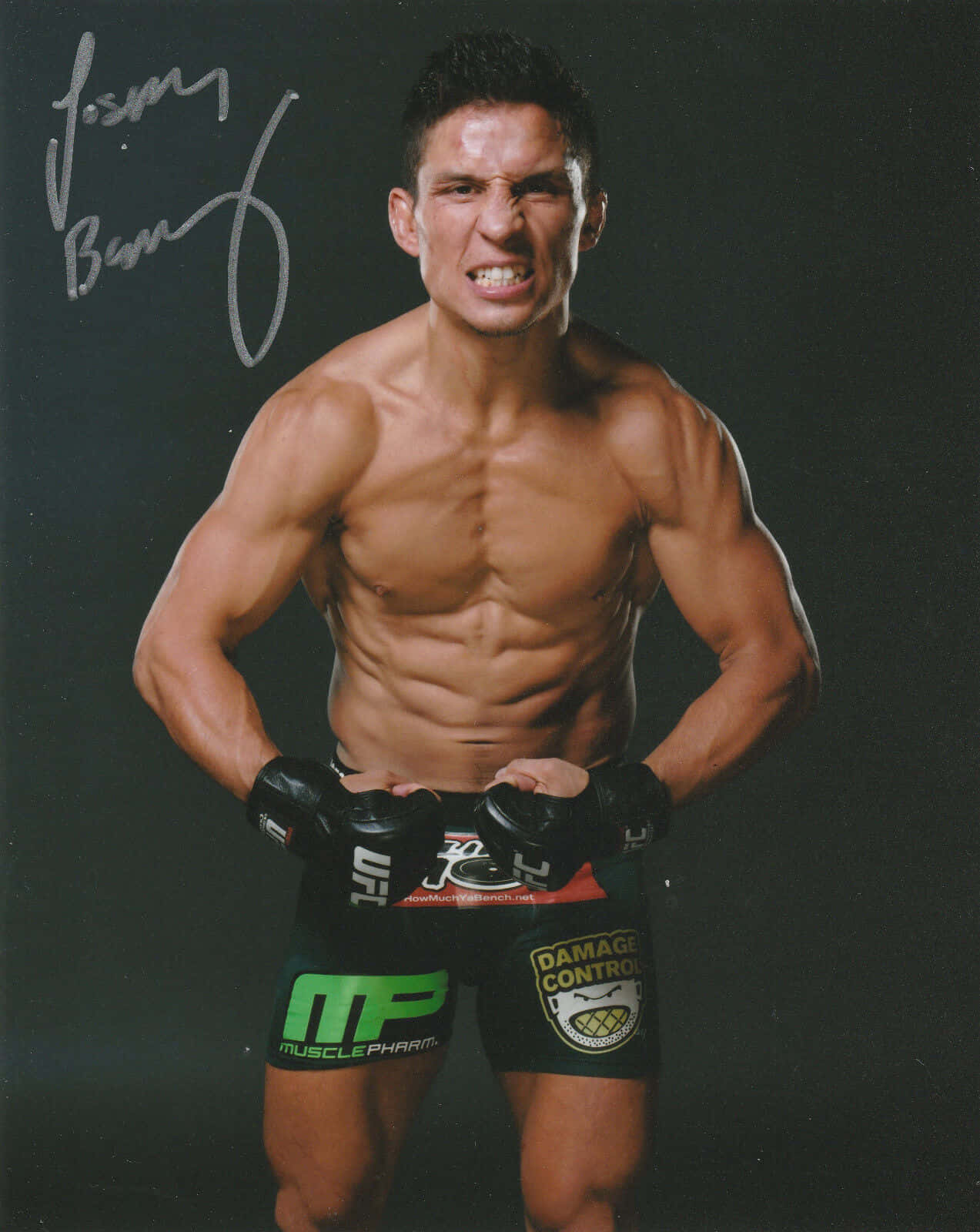 UFC 桌布 壁紙 — 一位肌肉發達的戰士穿著黑色短褲和手套，在黑暗的攝影棚背景下，露出他的簽名，表情猙獰。