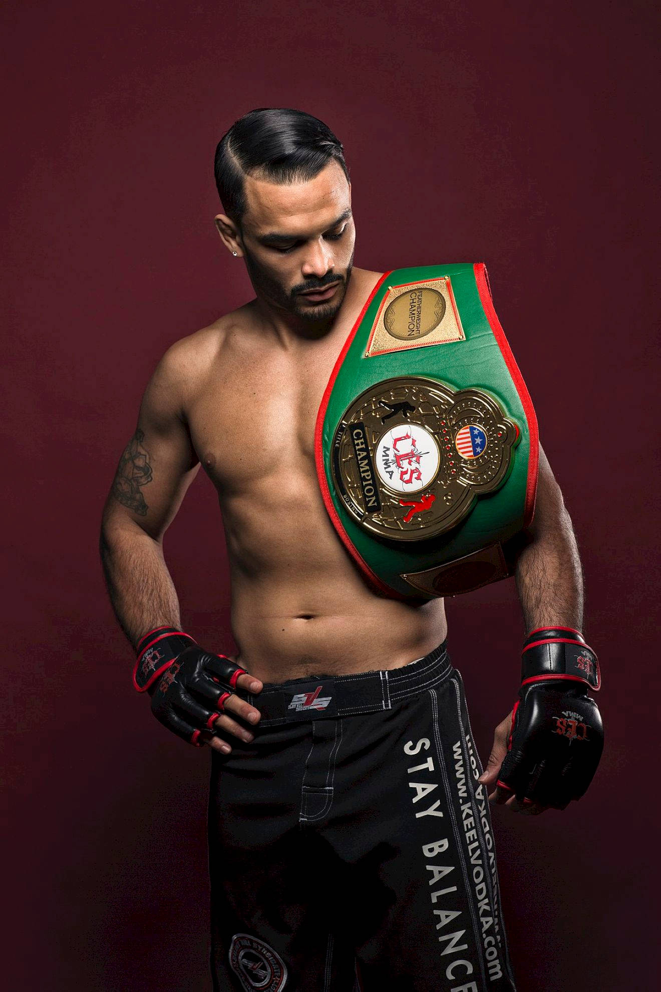 UFC 桌布 壁紙 — 一位肌肉發達的戰士穿著黑色短褲和手套，在深酒紅色的攝影棚背景前舉起一條綠色的冠軍腰帶。