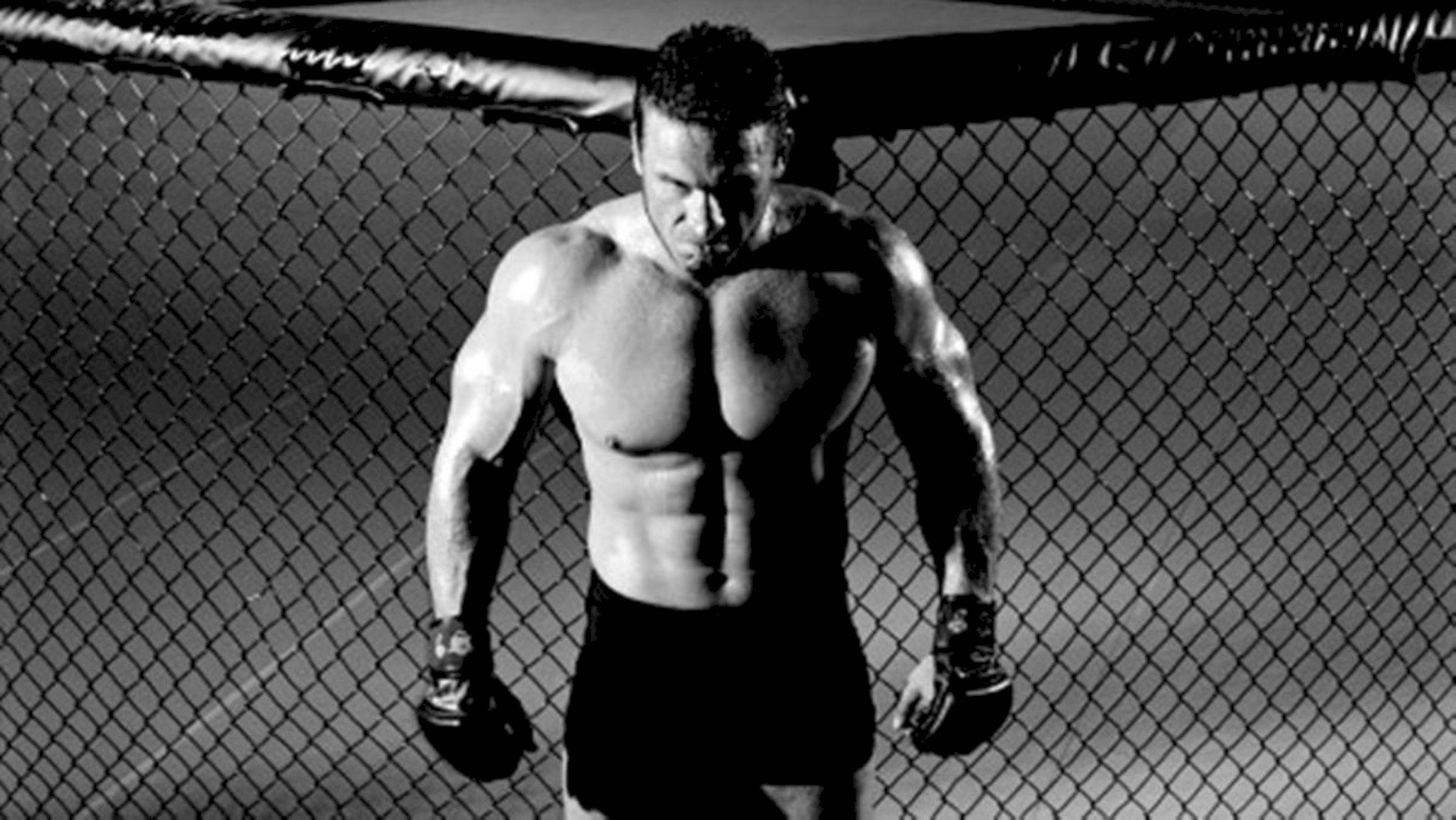 Fitness 桌布 壁紙 — 一位肌肉發達的戰士站在籠內，戴著手套，在黑白照片中展現強烈專注力。