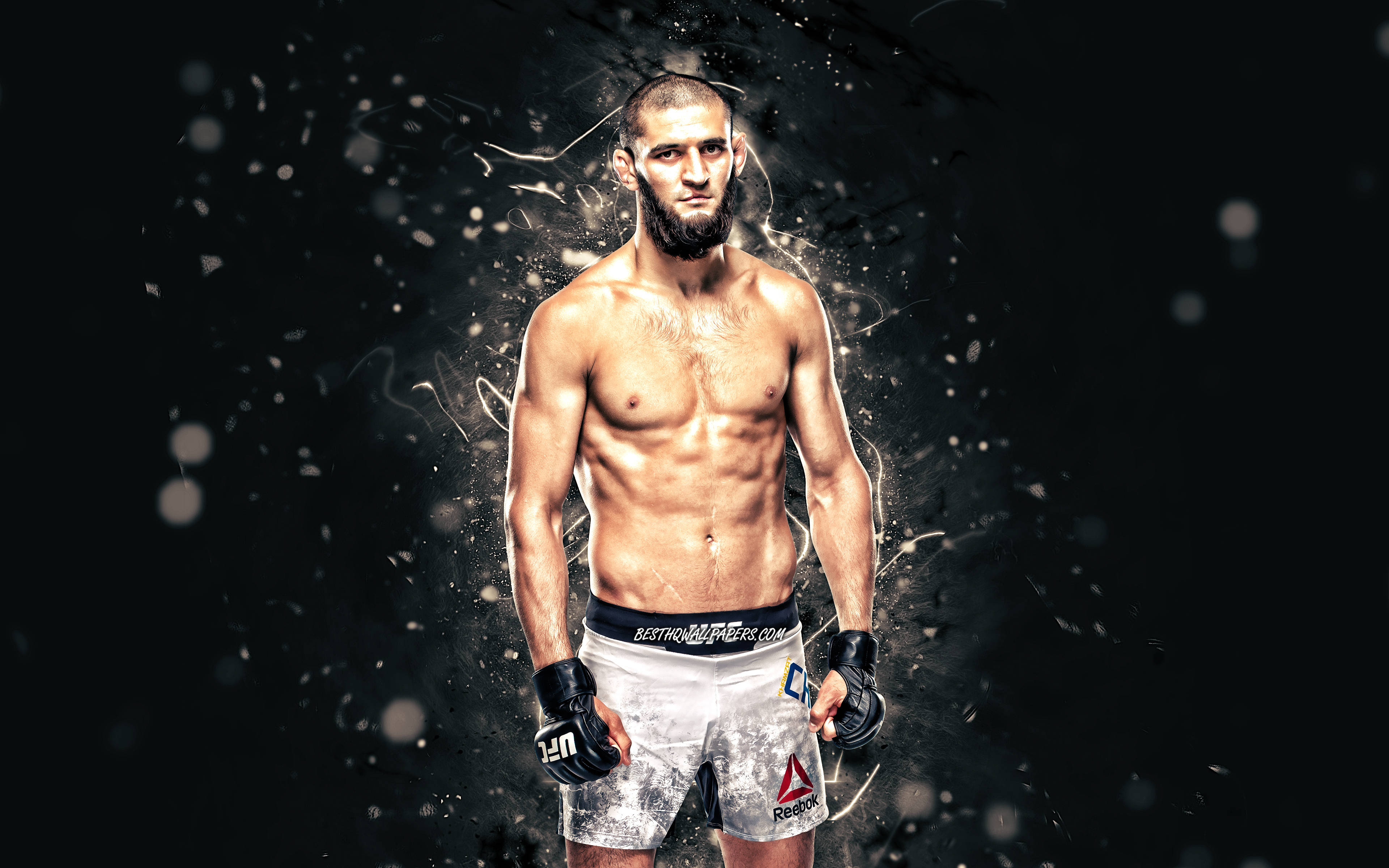 UFC 桌布 壁紙 — 一位肌肉發達的戰士自信地穿著戰鬥裝備，站在黑暗背景前，帶有發光粒子效果。