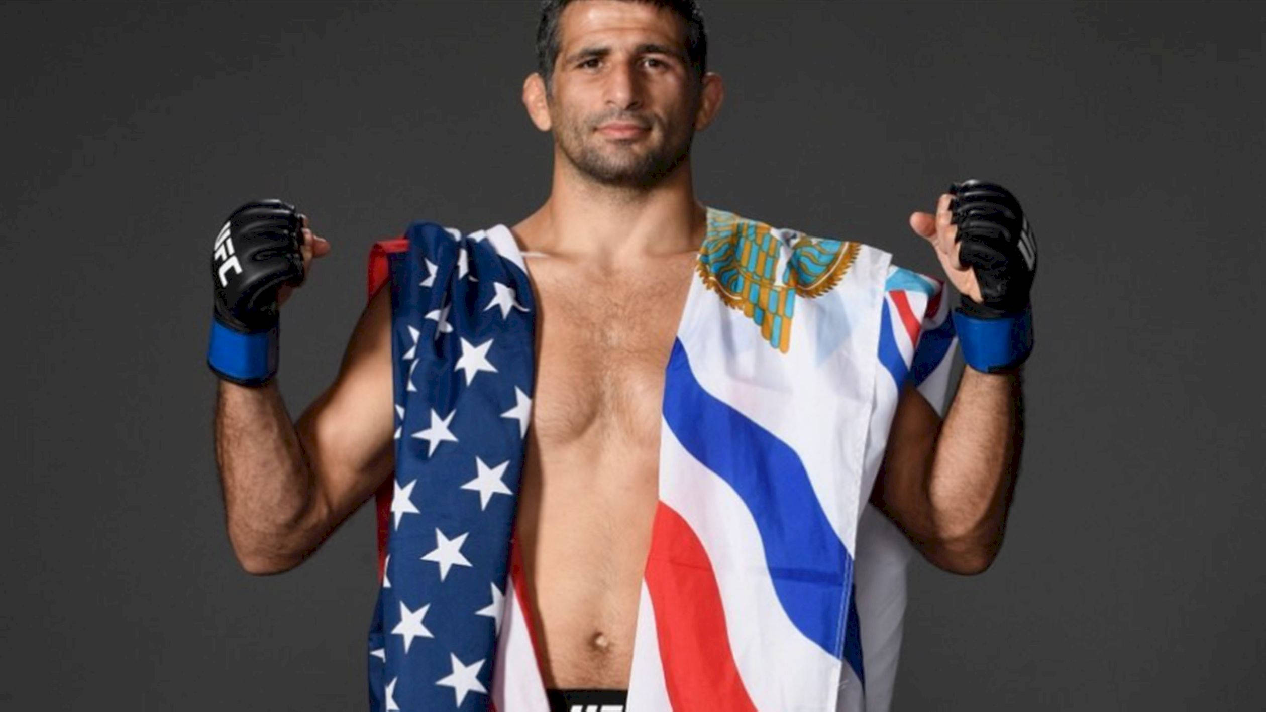 UFC 桌布 壁紙 — 一位肌肉發達的戰士自信地站立，披著美國和俄羅斯國旗，背景是黑暗的攝影棚。
