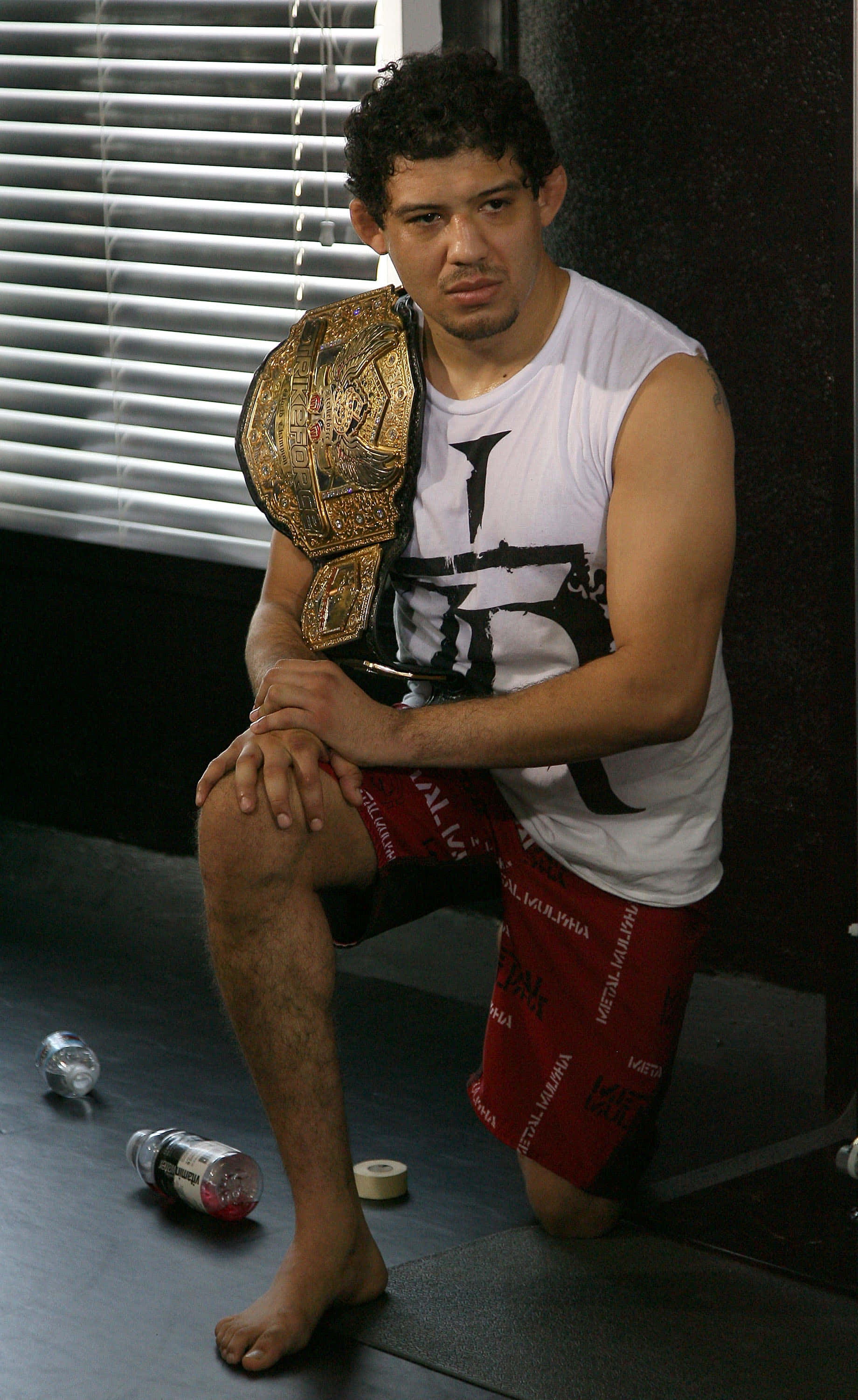 Champion 桌布 壁紙 — 一位肌肉發達的戰士赤腳坐在健身房地板上，專注地握著冠軍腰帶。