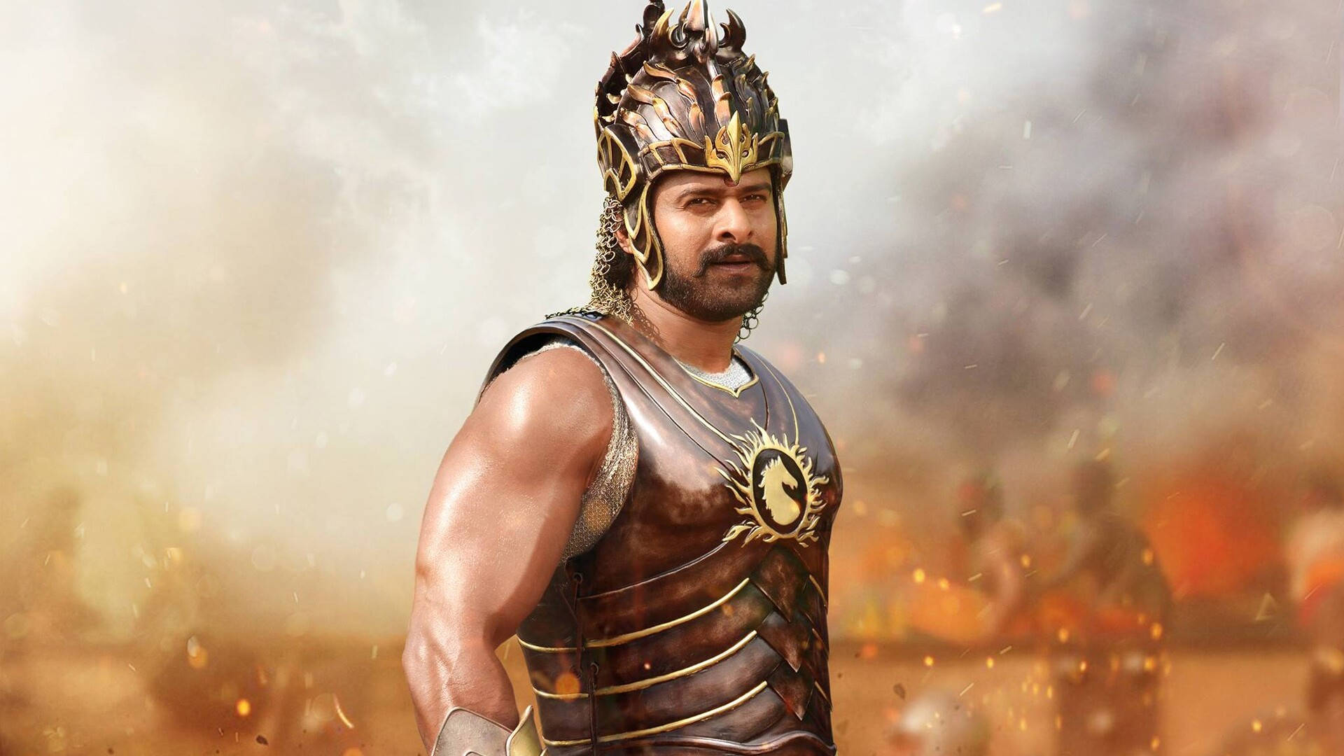 Prabhas HD 桌布 壁紙 — 一位肌肉發達的戰士身穿華麗的金色和青銅盔甲，在熾熱的戰鬥煙霧和飛舞的火花中挑釁地站立。