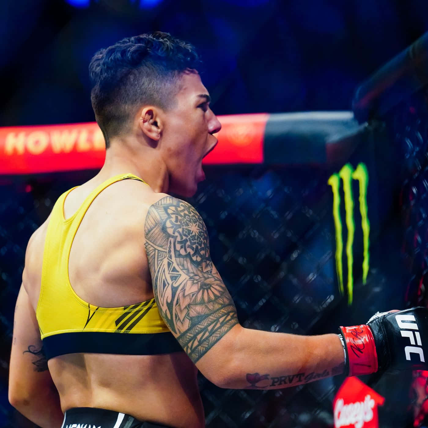 MMA 桌布 壁紙 — 一位肌肉發達的戰士身穿黃色上衣，在UFC八角籠內勝利咆哮，手臂上的刺青清晰可見。