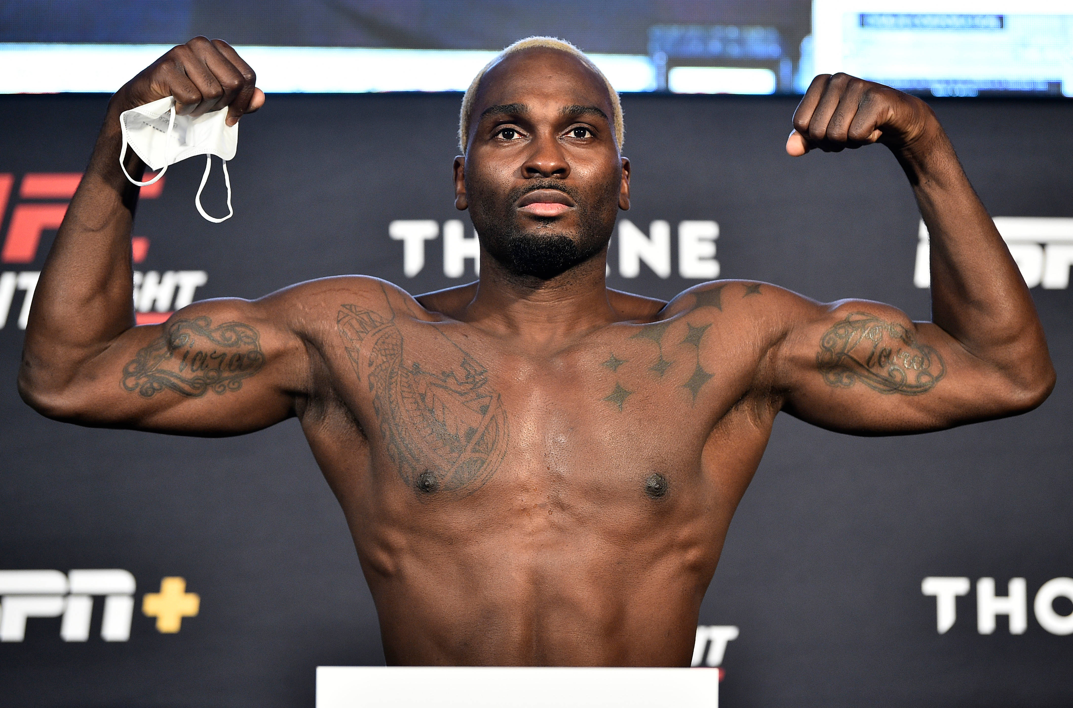 Champion 桌布 壁紙 — 一位肌肉發達的拳手在UFC品牌背景的稱重活動中，手持口罩並彎曲手臂。