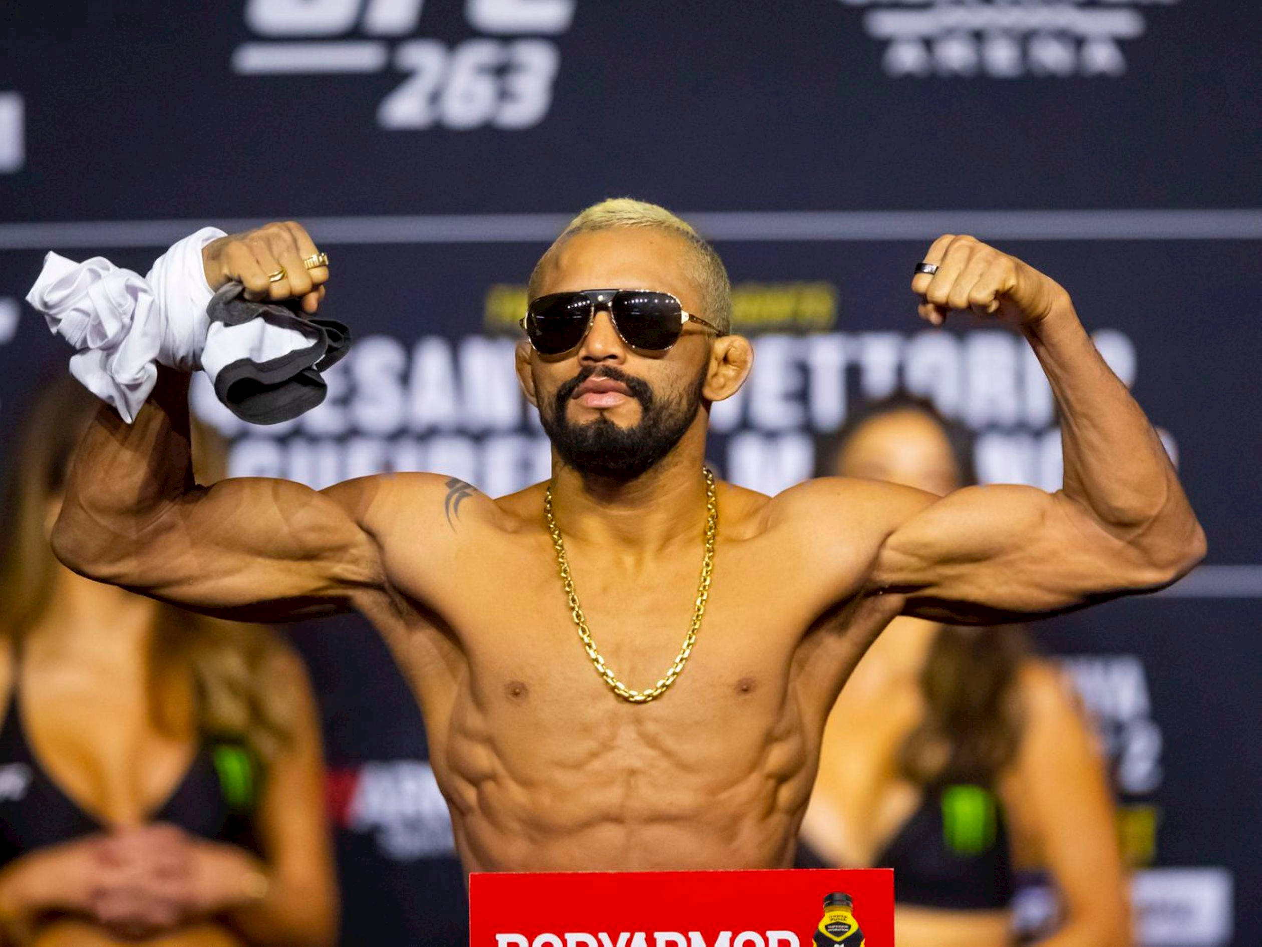 MMA 桌布 壁紙 — 一位肌肉發達的拳手在UFC稱重活動中戴著太陽眼鏡和金鍊，彎曲手臂展示肌肉。