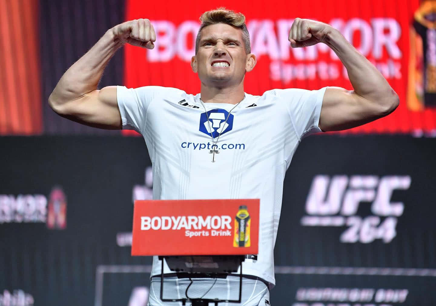 MMA 桌布 壁紙 — 一位肌肉發達的拳手在明亮的場館燈光下，於 UFC 稱重活動中露出兇猛的笑容，彎曲二頭肌。