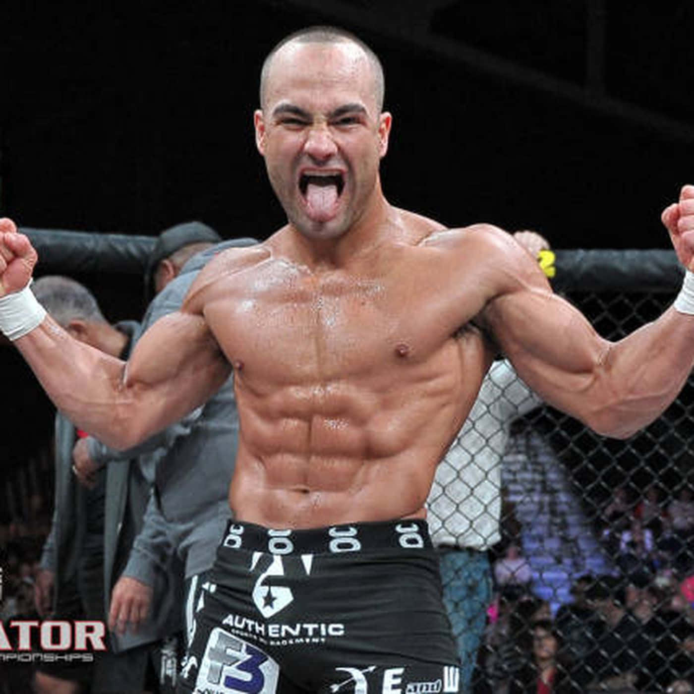 UFC 桌布 壁紙 — 一位肌肉發達的拳手在明亮的場館燈光下，於籠中高舉拳頭、伸出舌頭慶祝勝利。