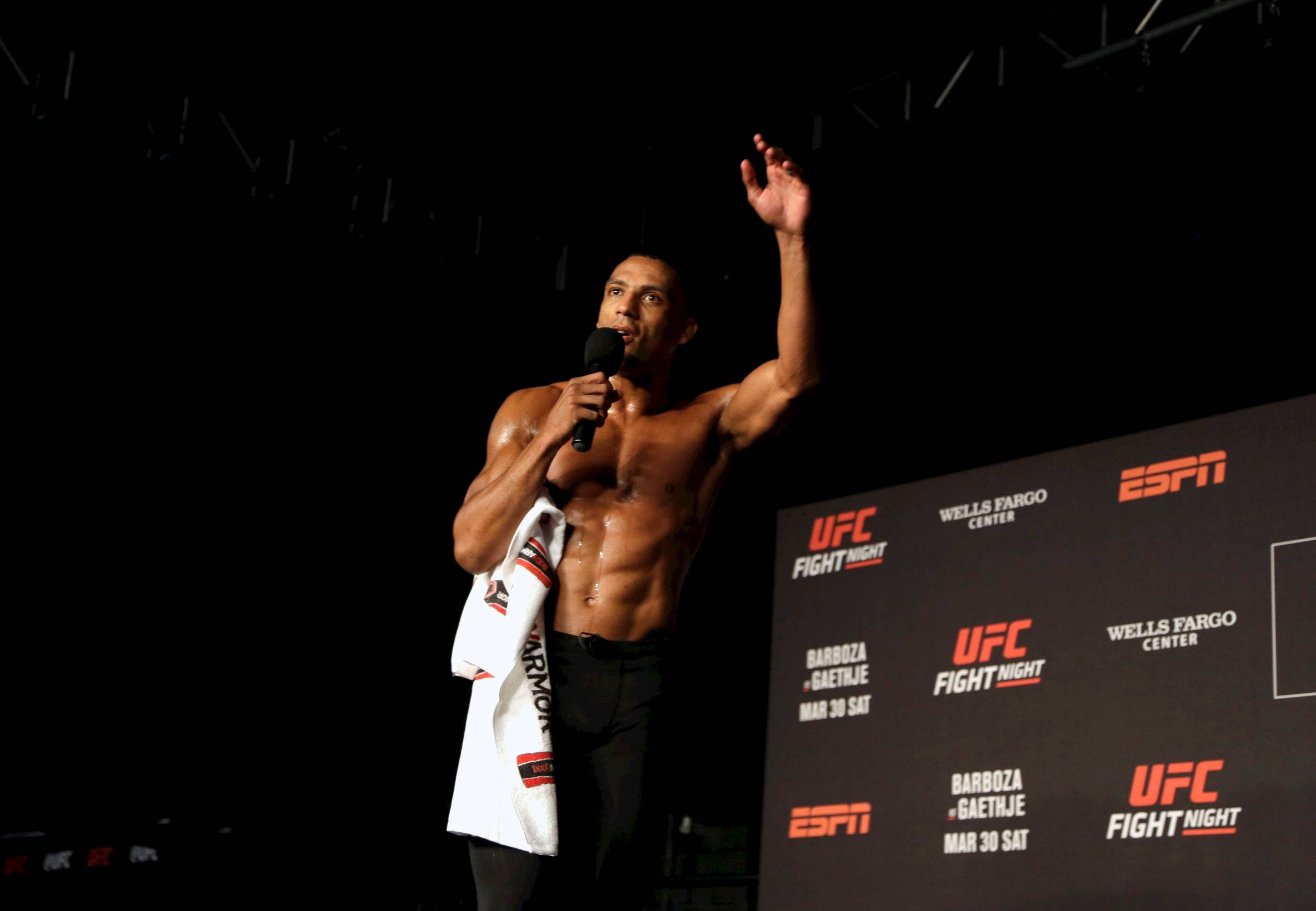 MMA 桌布 壁紙 — 一位肌肉發達的拳手在明亮的燈光下，在UFC舞台上拿著麥克風向粉絲揮手。