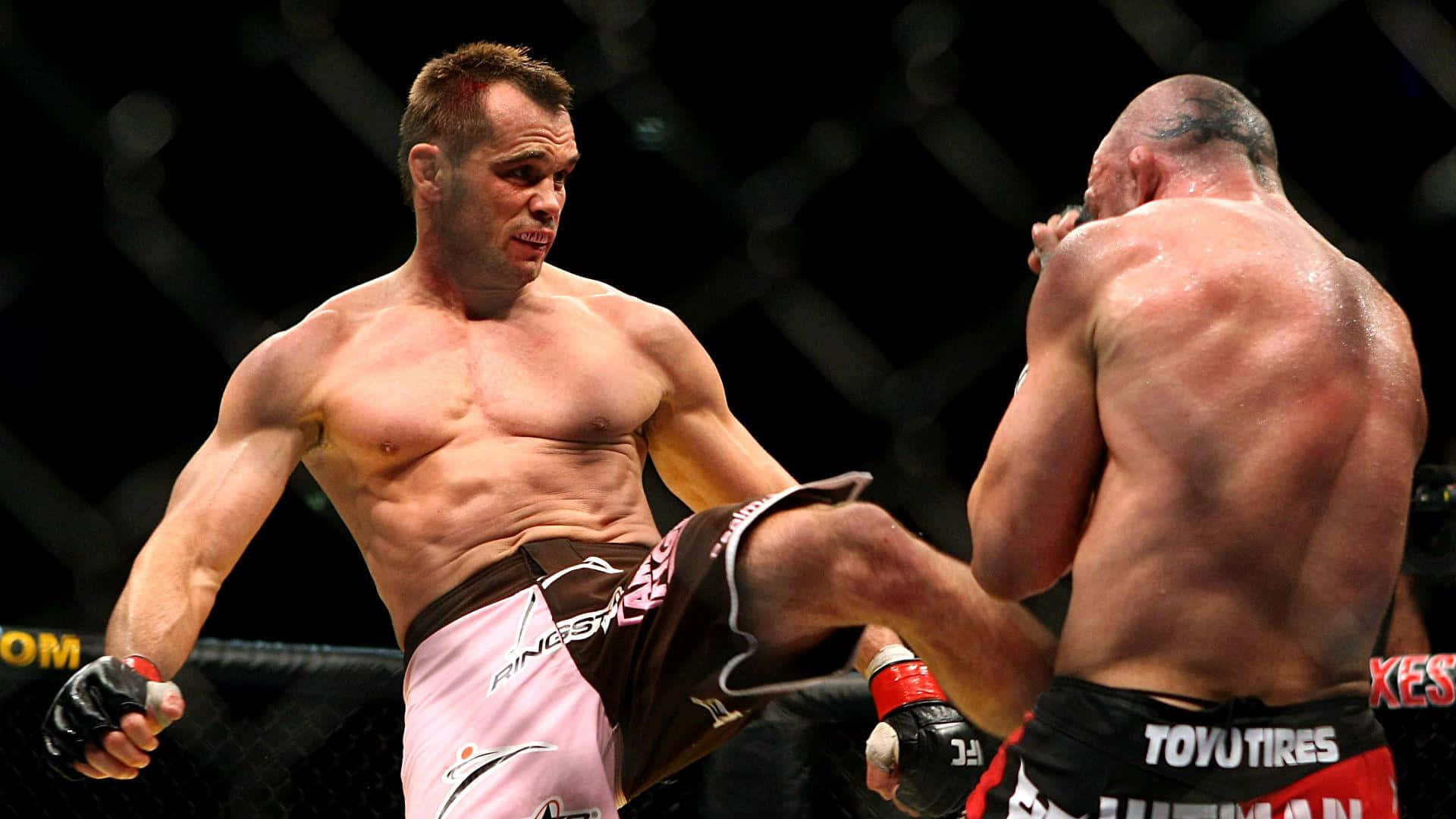 UFC 桌布 壁紙 — 一位肌肉發達的拳手在昏暗的MMA籠中進行激烈比賽時，向對手踢出一記高踢。