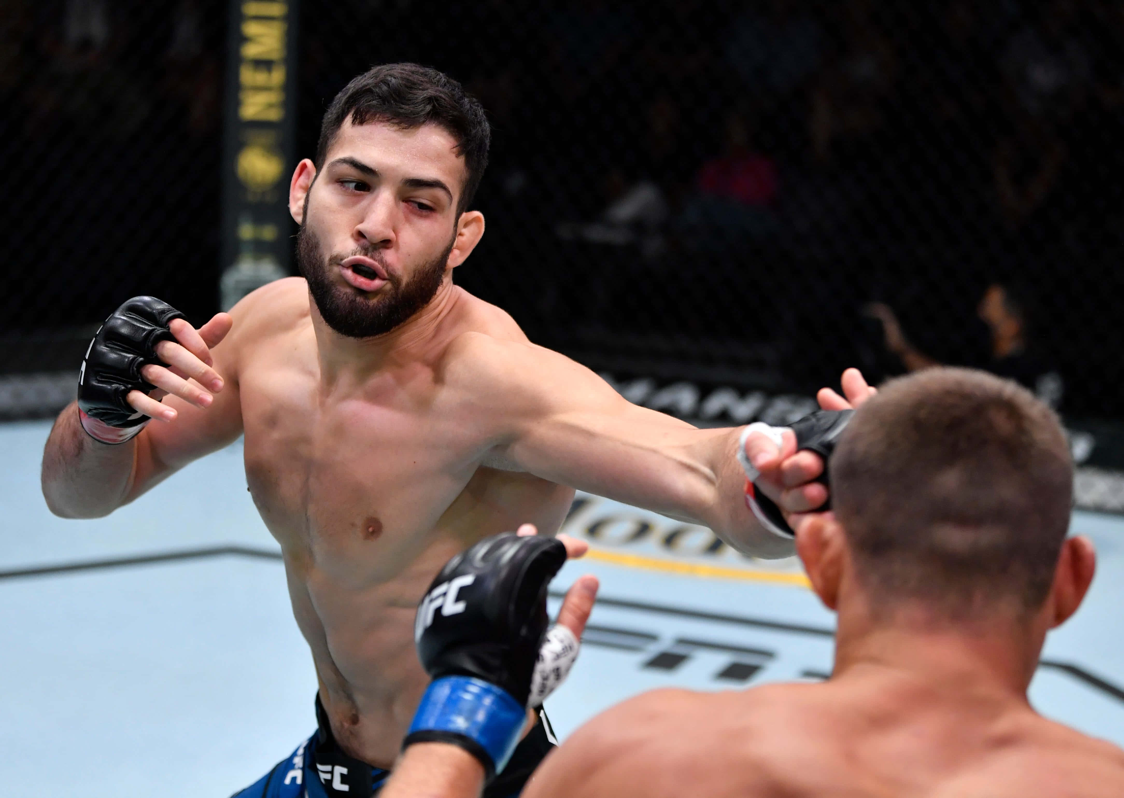UFC 桌布 壁紙 — 一位肌肉發達的拳手在燈光明亮的MMA八角籠中打出強力一拳，背景是模糊的觀眾。