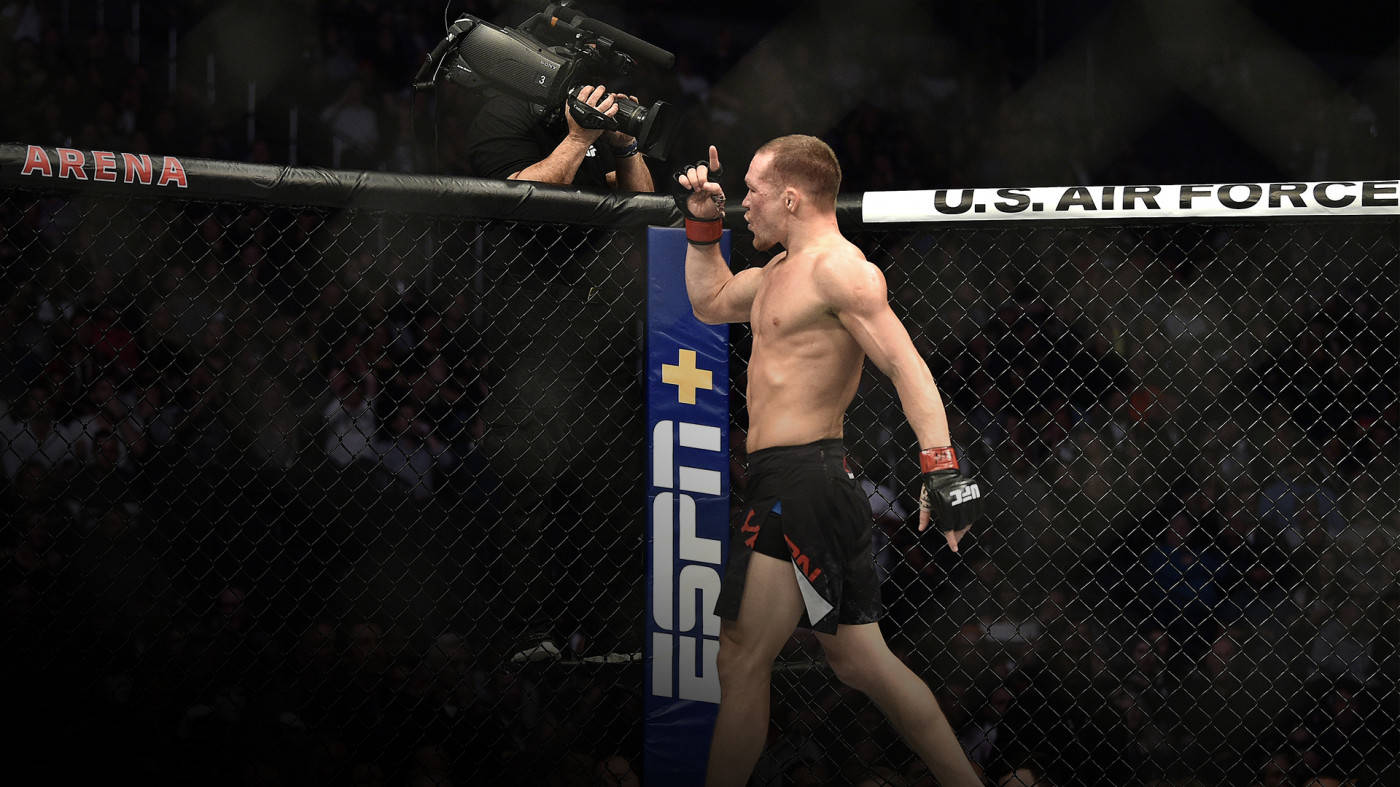 Petr Yan 桌布 壁紙 — 一位肌肉發達的拳手在燈光昏暗的MMA八角籠中慶祝勝利，場地帶有ESPN品牌標誌和美國空軍贊助。