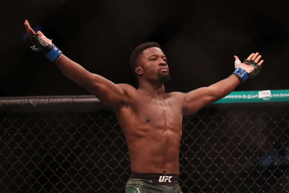 UFC 桌布 壁紙 — 一位肌肉發達的拳手在燈光昏暗的UFC八角籠內高舉雙臂慶祝勝利。