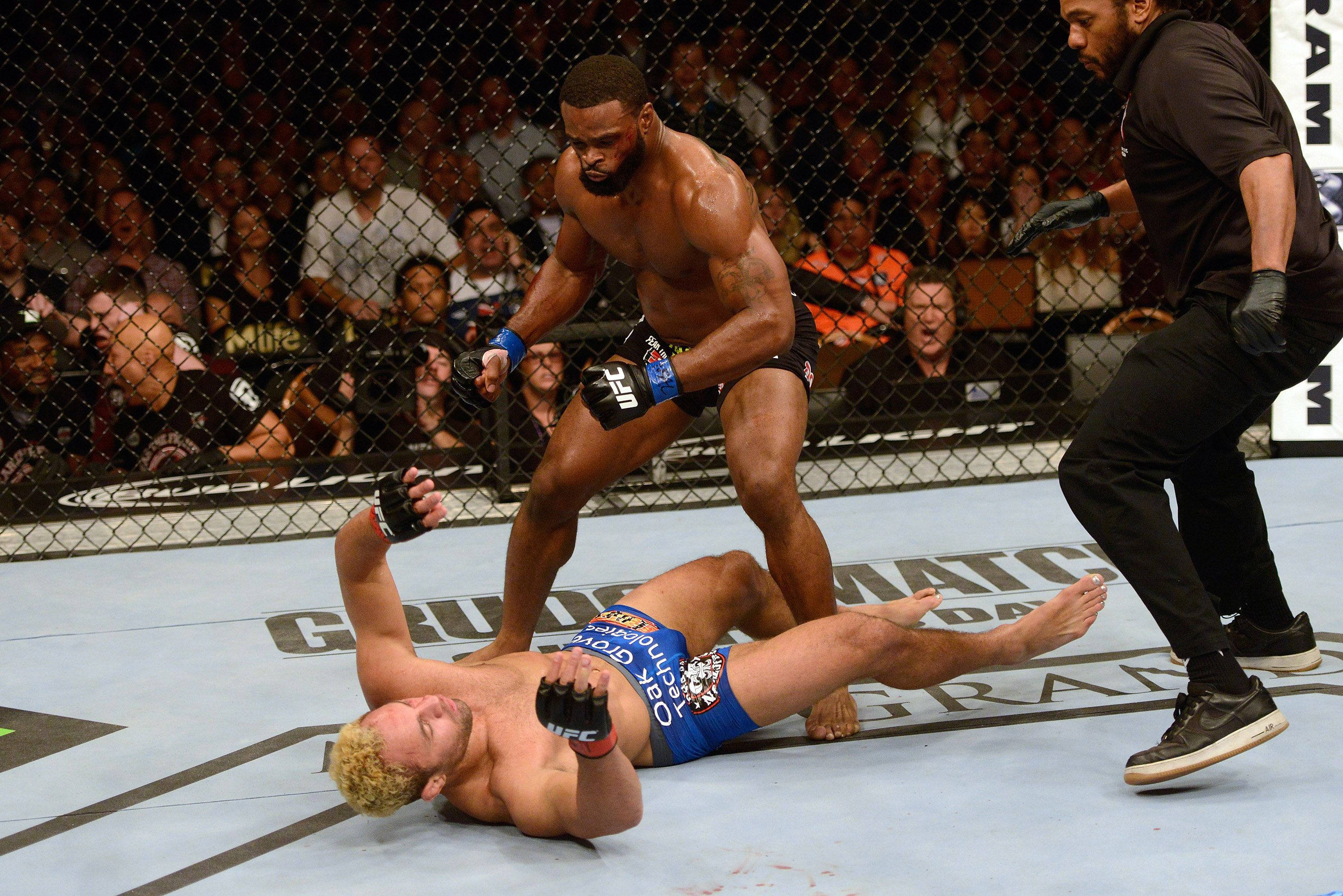 Tyron Woodley 桌布 壁紙 — 一位肌肉發達的拳手在燈光通明的MMA八角籠中壓制對手在地面，裁判在附近。