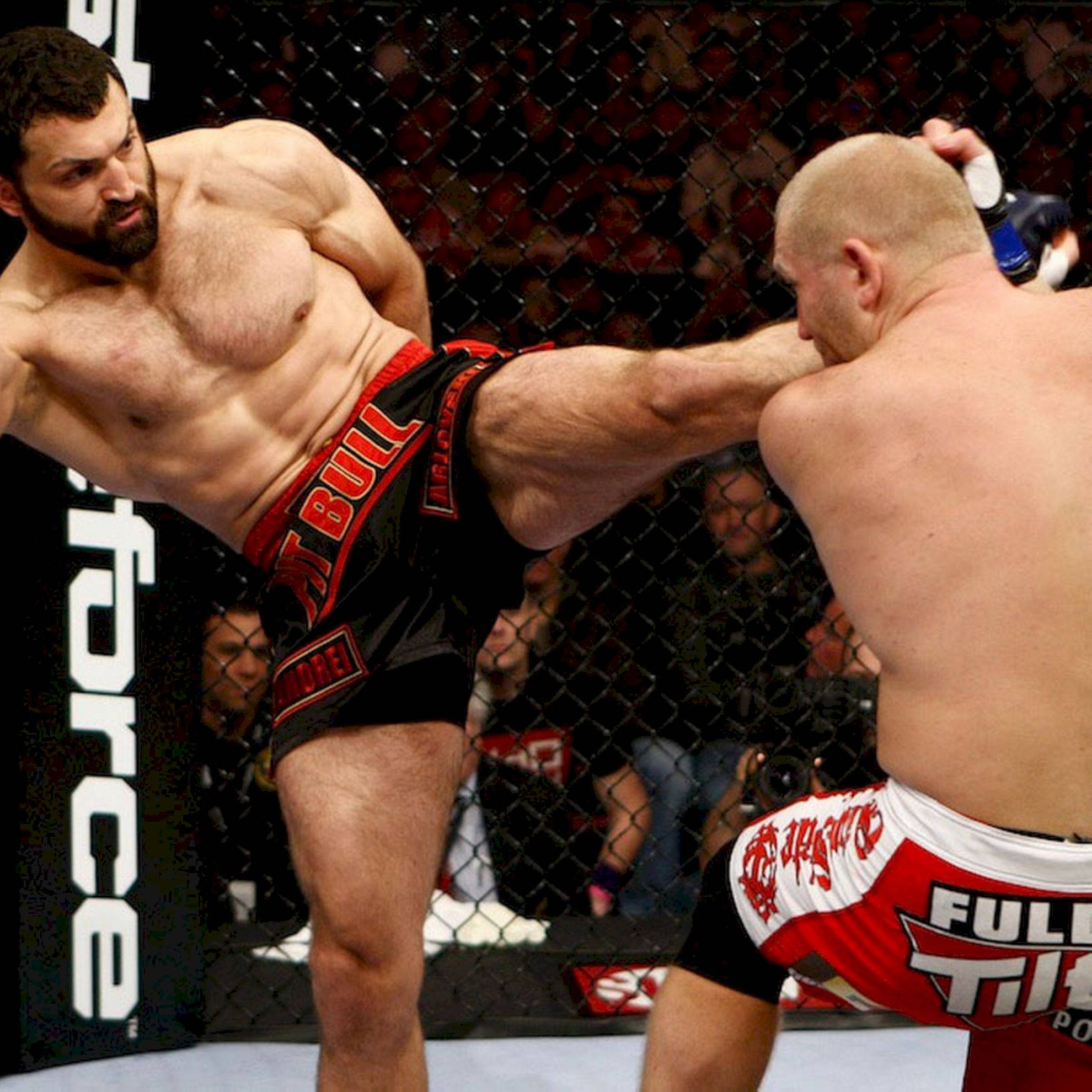 UFC 桌布 壁紙 — 一位肌肉發達的拳手在現場活動中於綜合格鬥籠內向對手踢出高踢。