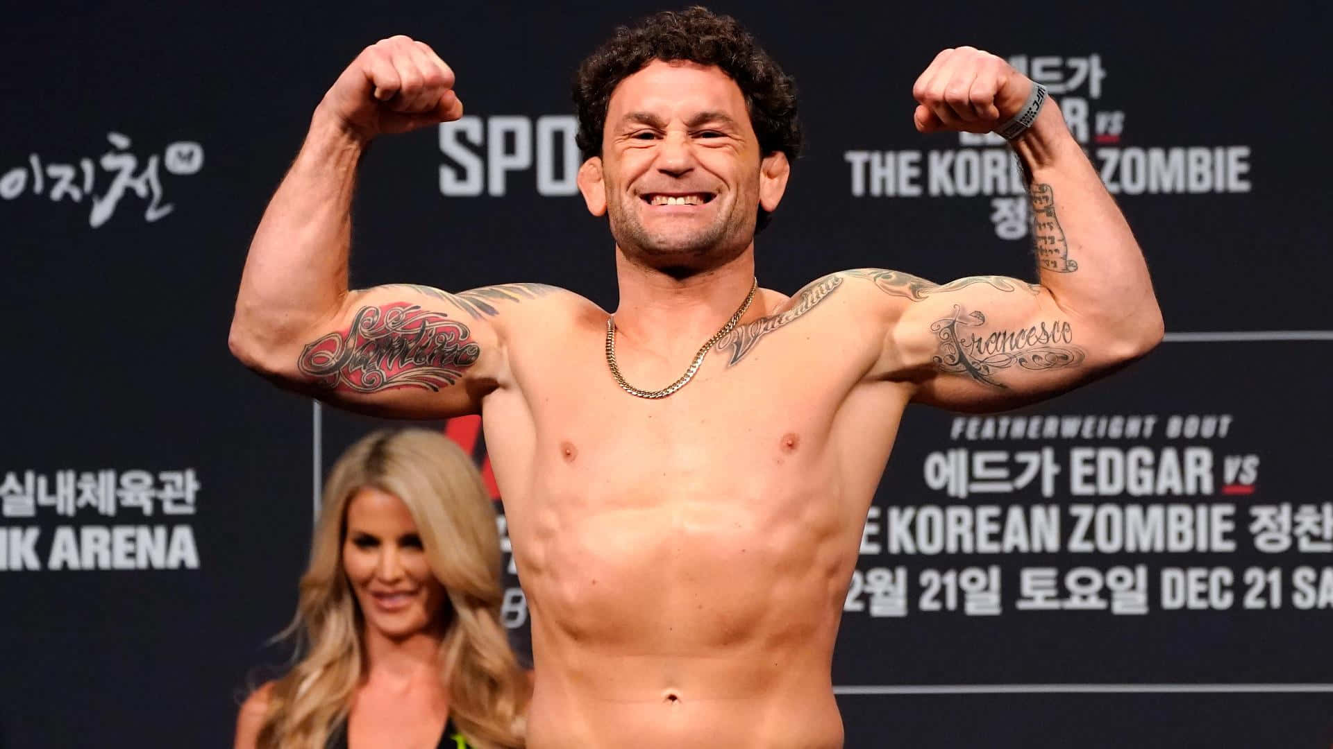 UFC 桌布 壁紙 — 一位肌肉發達的拳手在稱重活動中彎曲雙臂，露出紋身，微笑著。