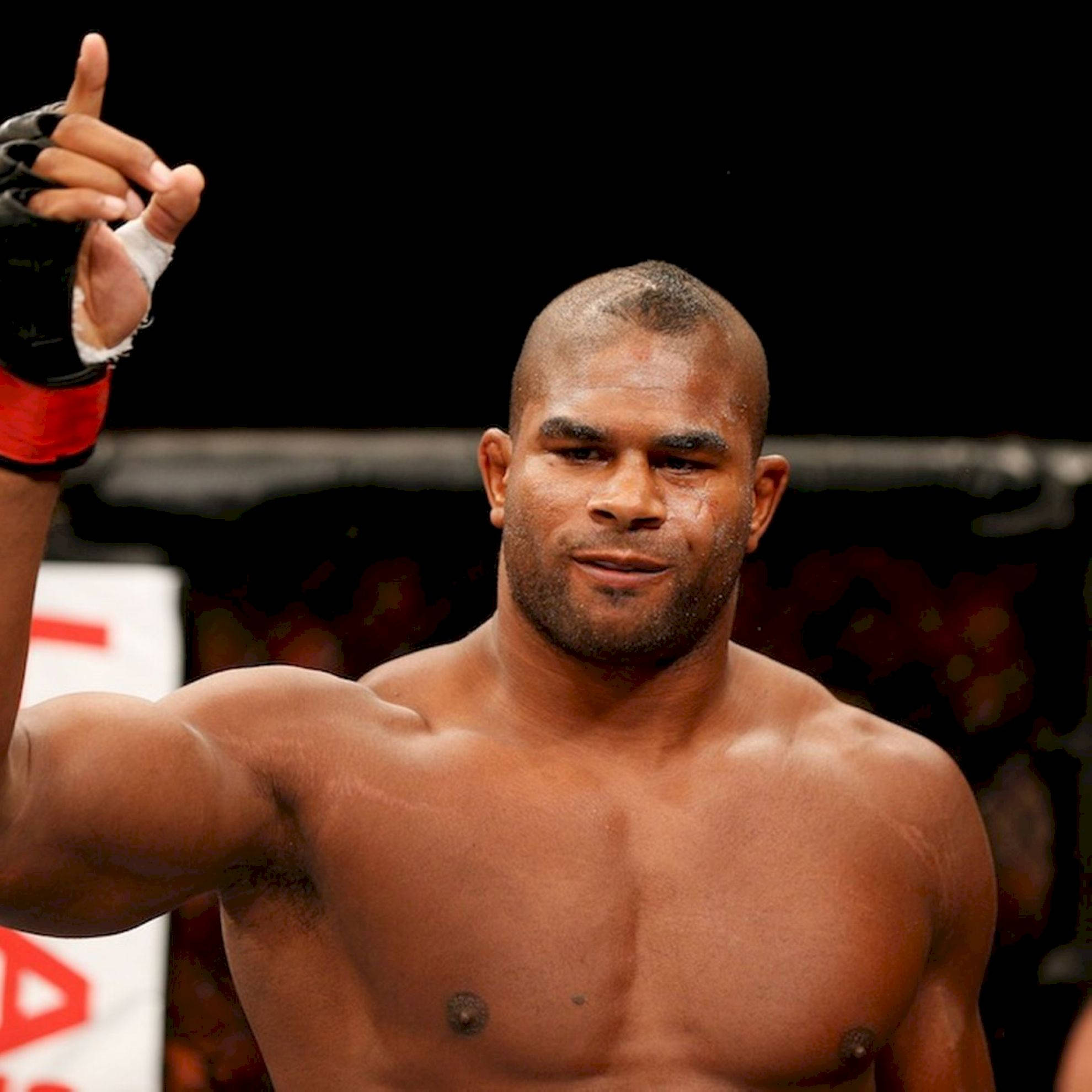 UFC 桌布 壁紙 — 一位肌肉發達的拳手在籠中自信地微笑，舉起戴著手套的手慶祝勝利。