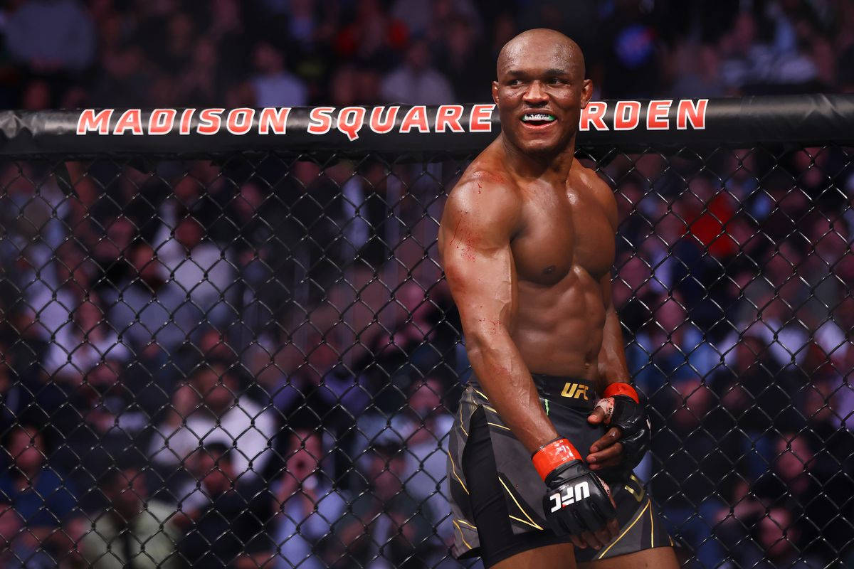 UFC 桌布 壁紙 — 一位肌肉發達的拳手在麥迪遜廣場花園的UFC八角籠內，圍欄後有群眾，露出勝利的笑容。