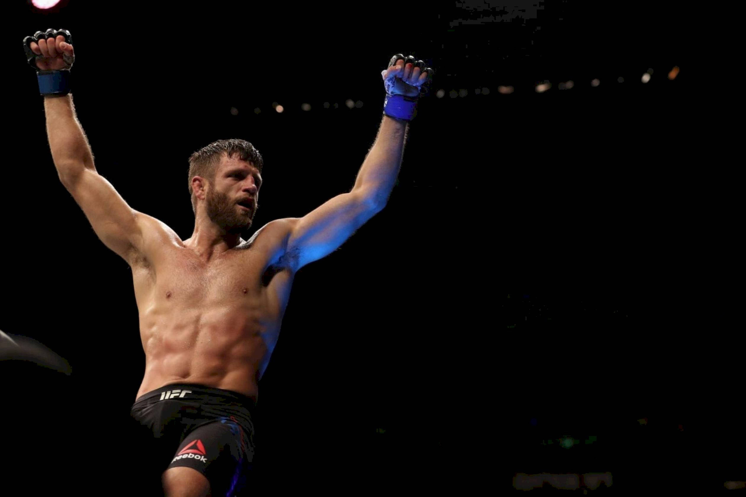 UFC 桌布 壁紙 — 一位肌肉發達的拳手在黑暗背景下，於競技場燈光下勝利地高舉戴著手套的拳頭。