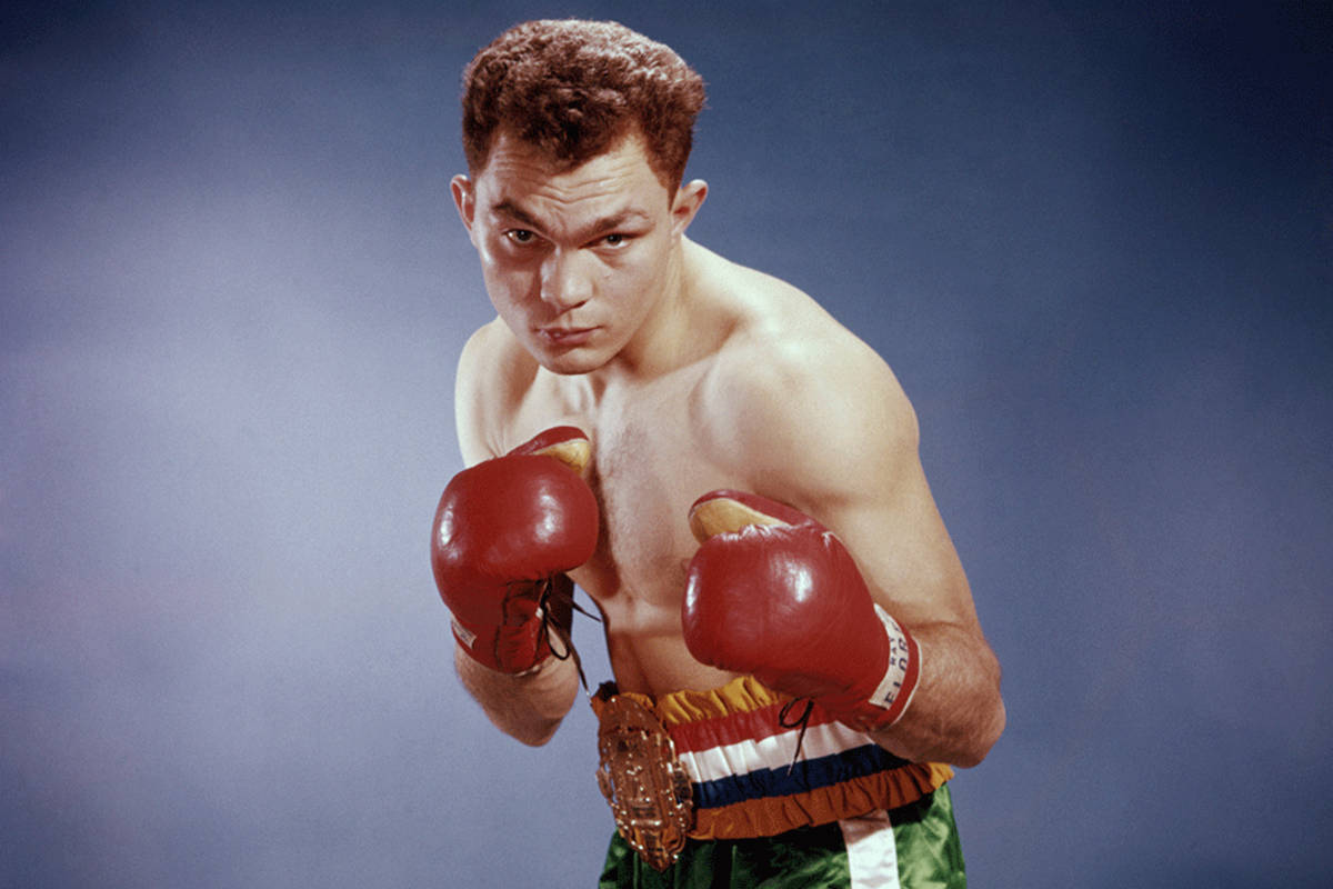 Boxing 桌布 壁紙 — 一位肌肉發達的拳擊手，戴著紅色手套和綠色短褲，在煙霧繚繞的藍色工作室背景下，舉起拳頭，目光專注。
