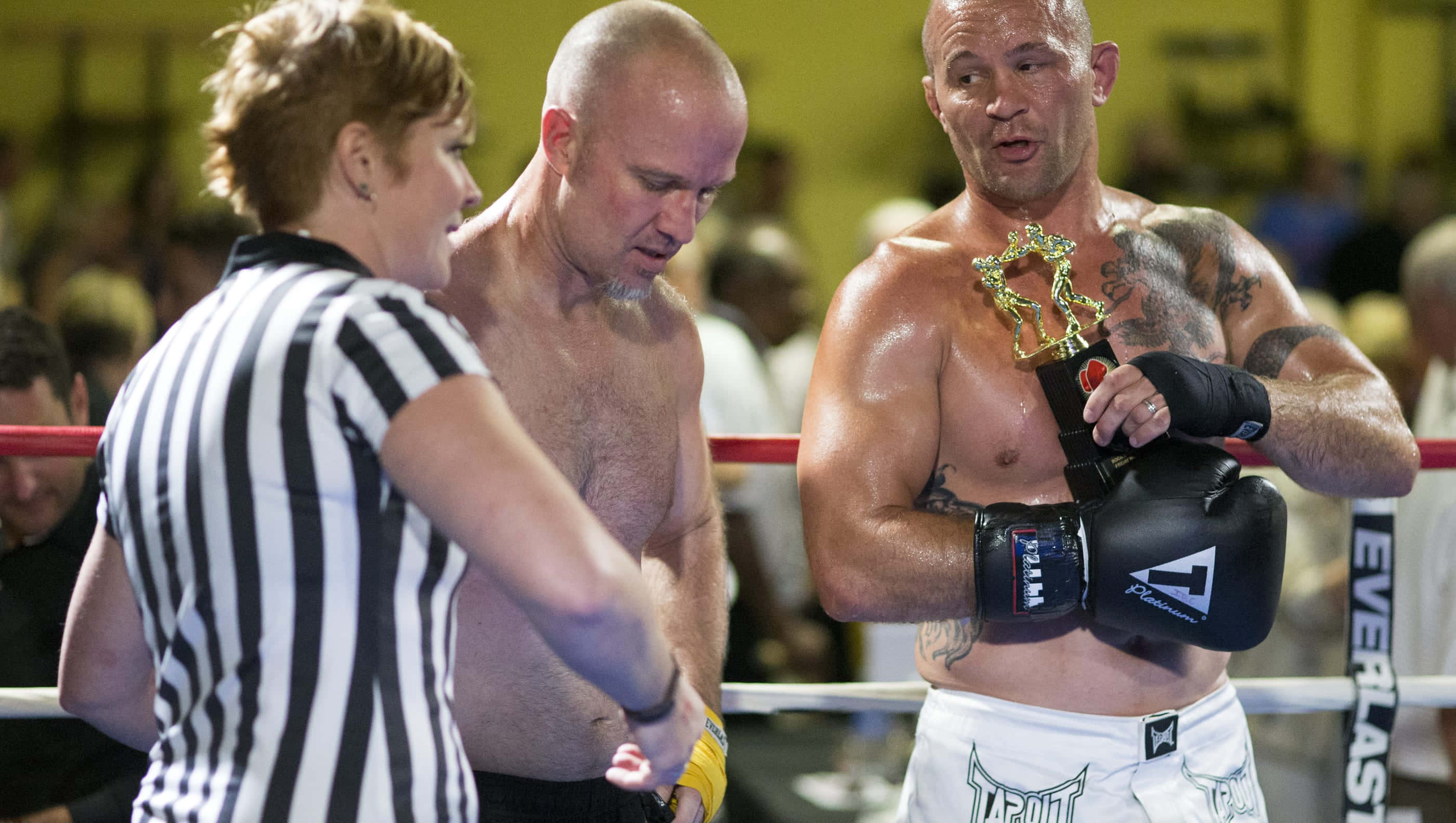 UFC 桌布 壁紙 — 一位肌肉發達的拳擊手在擂台上舉起冠軍獎盃，裁判和教練在比賽期間觀看。
