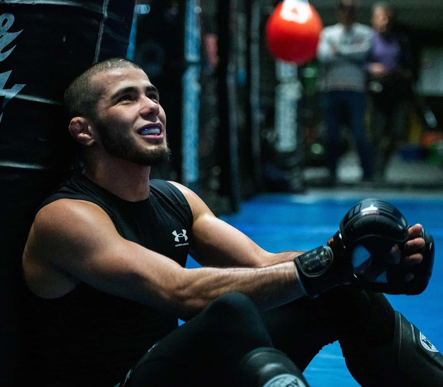 UFC 桌布 壁紙 — 一位肌肉發達的拳擊手在燈光昏暗的健身房裡靠著一個沉重的沙包休息，附近掛著一個紅色的藥球。